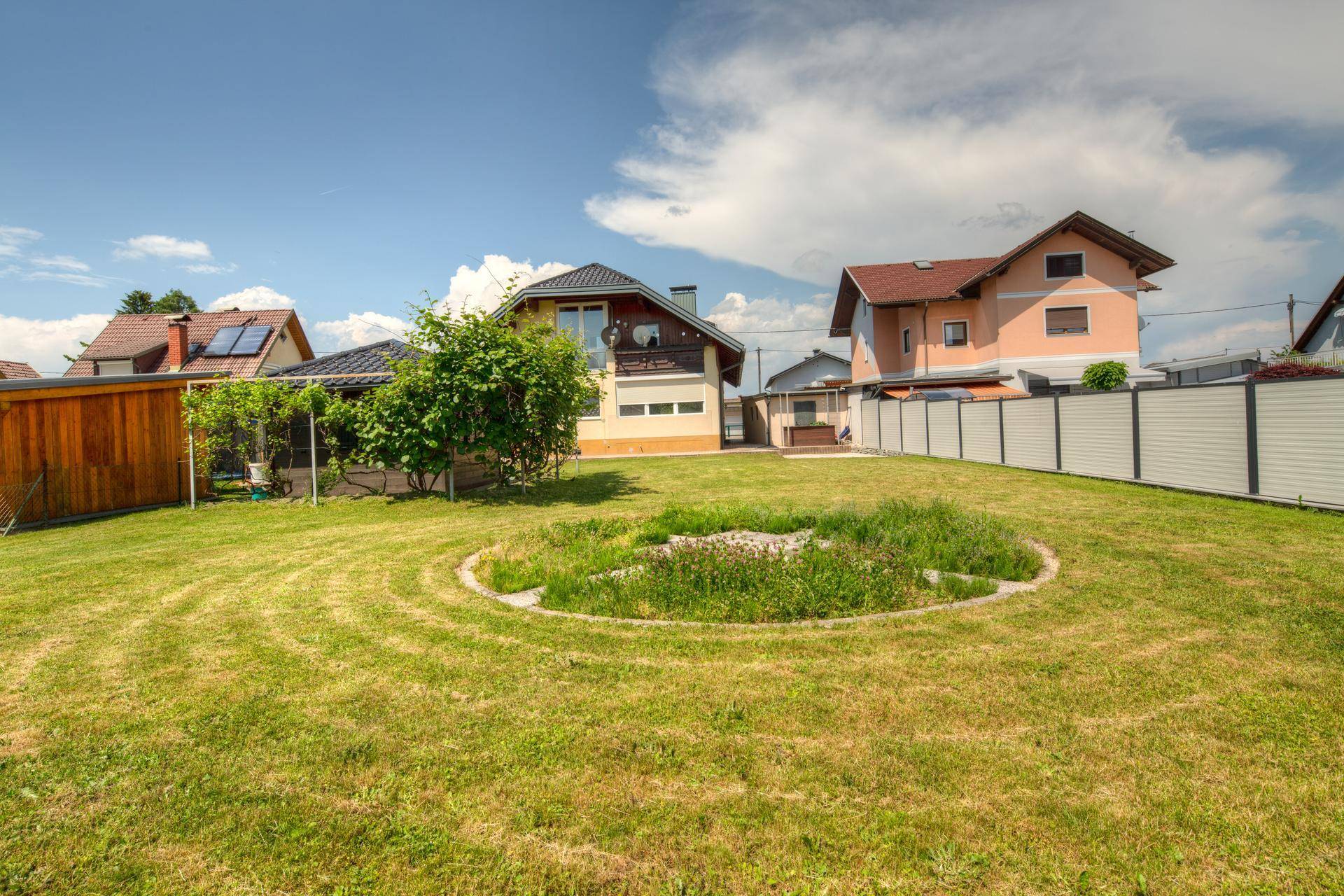 Weitläufiger Garten mit Rasenfläche und einer kreisförmigen Bepflanzung oder einem Teich.
