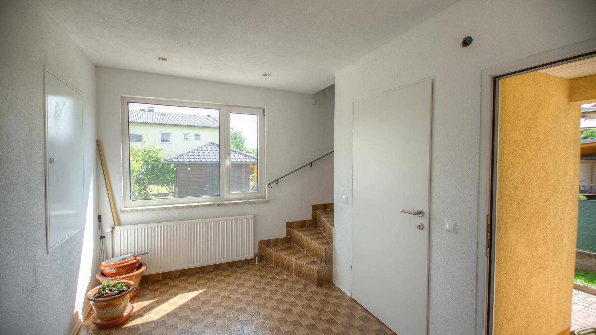 Heller Eingangsbereich mit Fliesenboden, Treppe und Blick auf den gepflegten Garten.