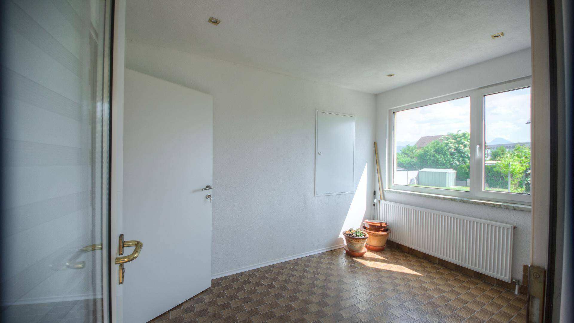 Heller Eingangsbereich mit Fliesenboden, Fenster und Blick auf den Gartenbereich.
