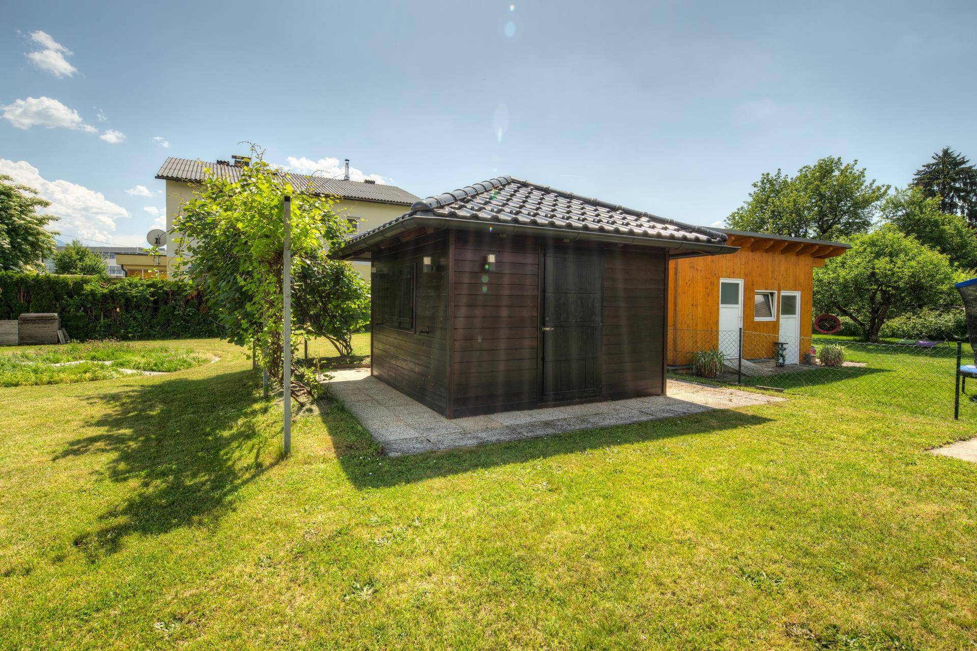 Kleines, dunkles Holzgartenhaus mit Satteldach auf einer grünen Rasenfläche.