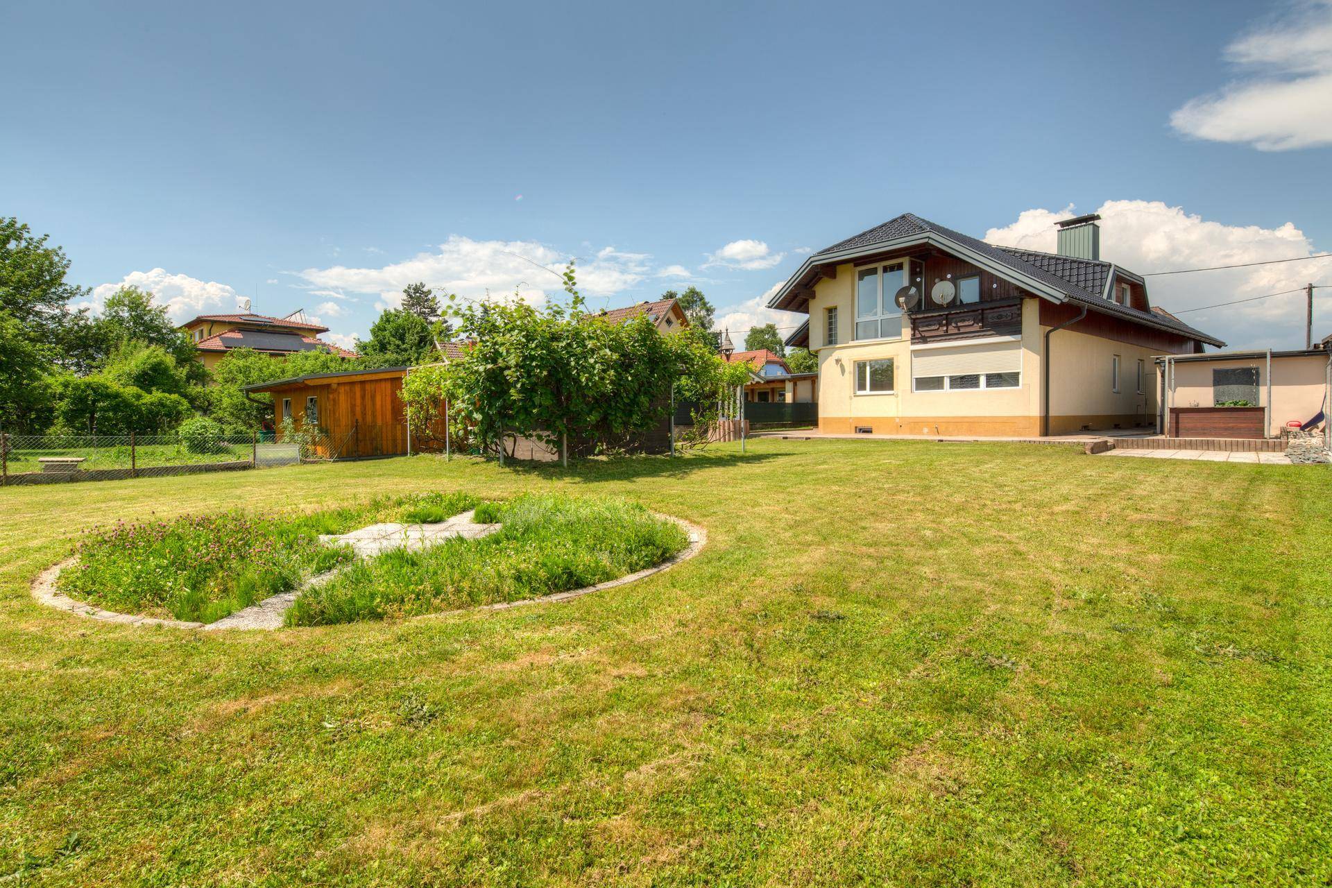 Großer Garten mit gepflegtem Rasen und einer runden Blumeninsel oder Teichanlage.
