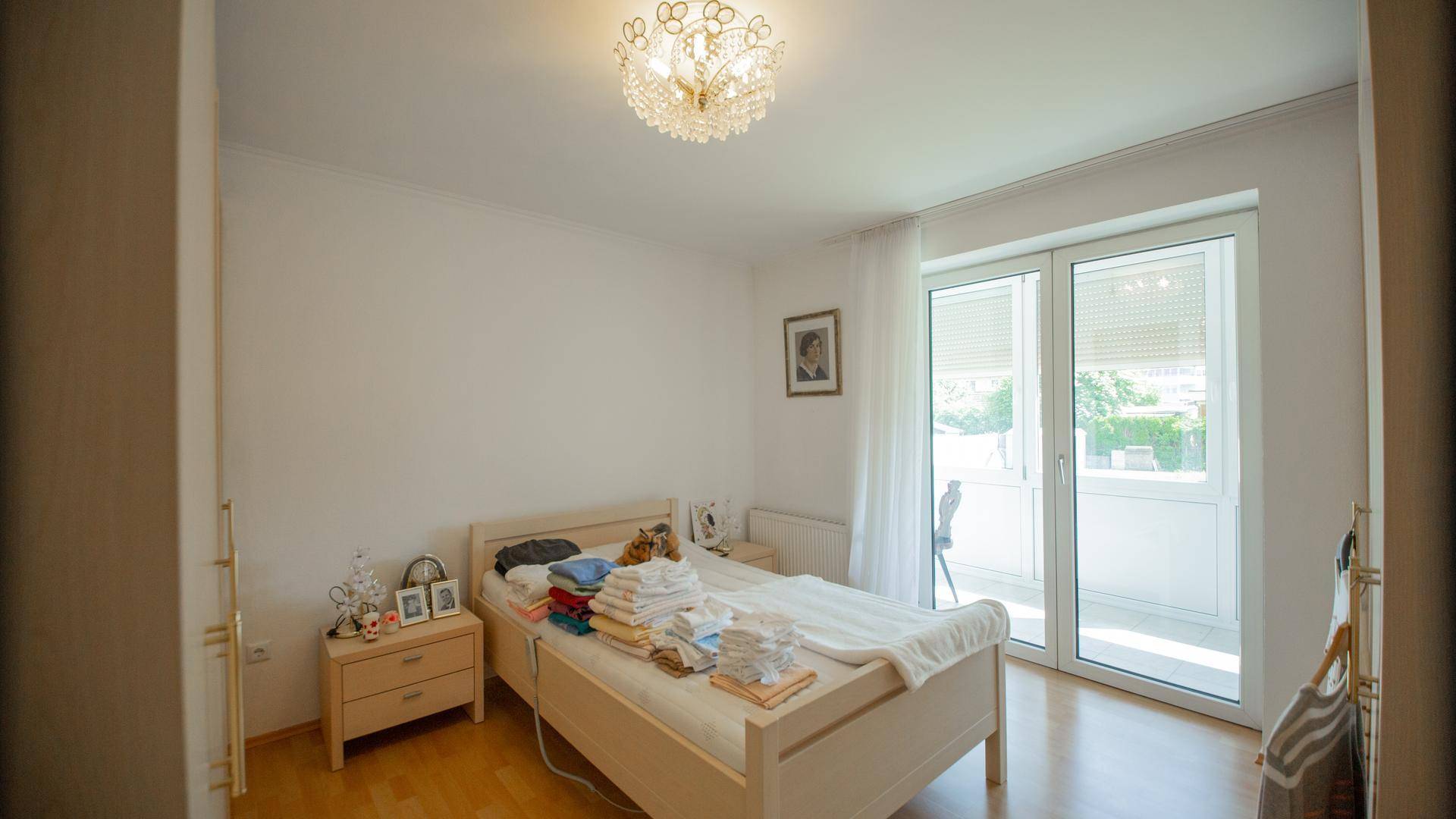 Schlafzimmer mit Doppelbett, Holzboden und direktem Zugang zum sonnigen Balkon.