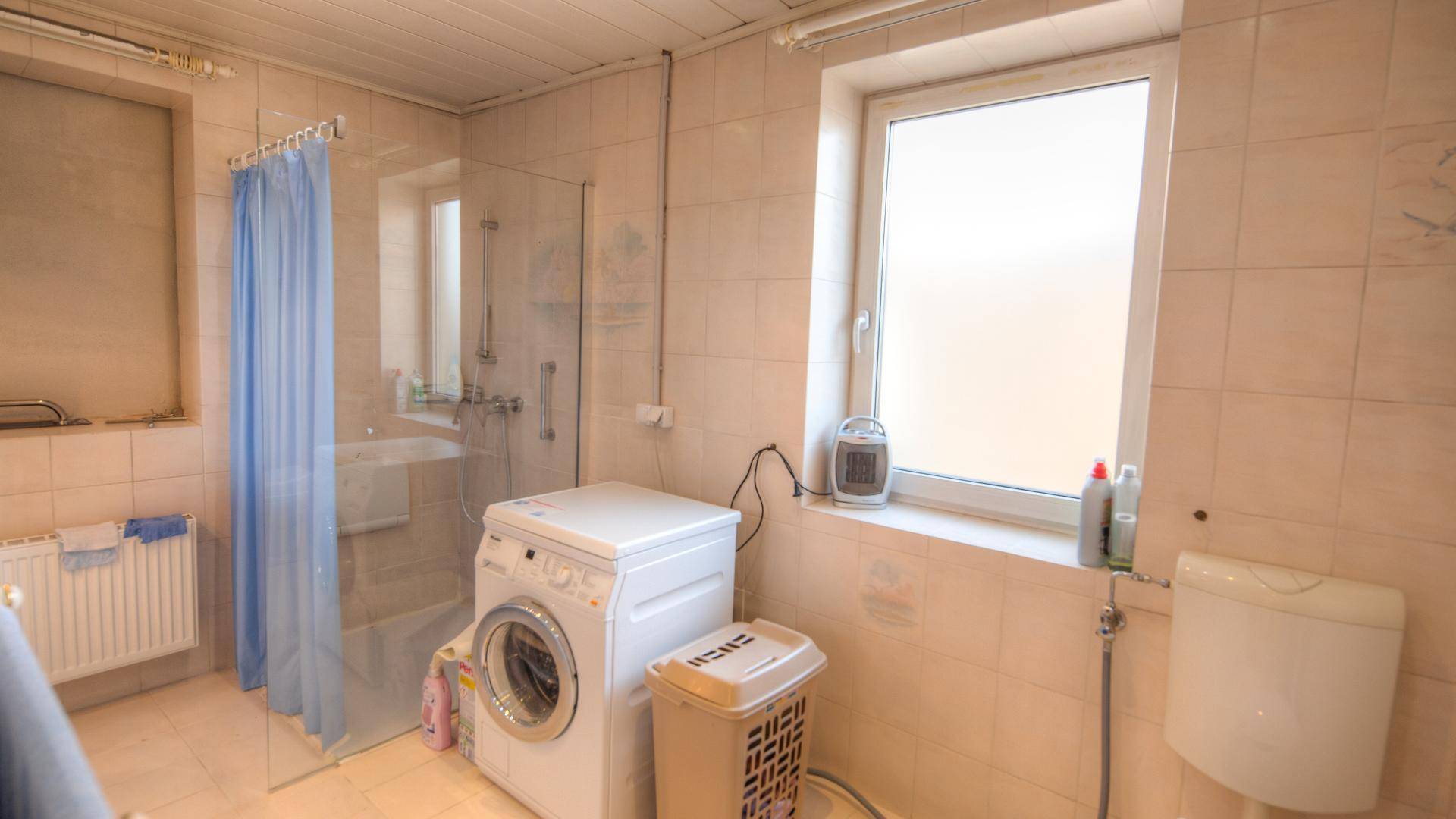 Funktionales Badezimmer mit Dusche, WC, Waschmaschine und einem Fenster für Tageslicht.