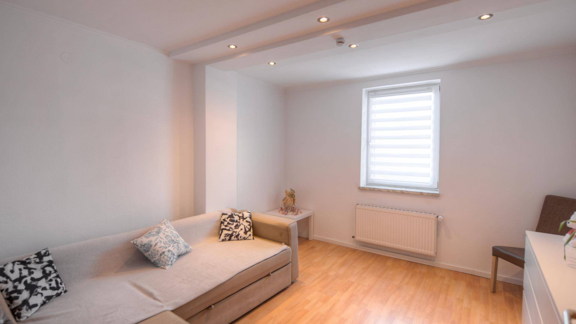 Helles Wohnzimmer mit beigem Sofa, Holzboden und Deckenstrahlern für gemütliche Abende.