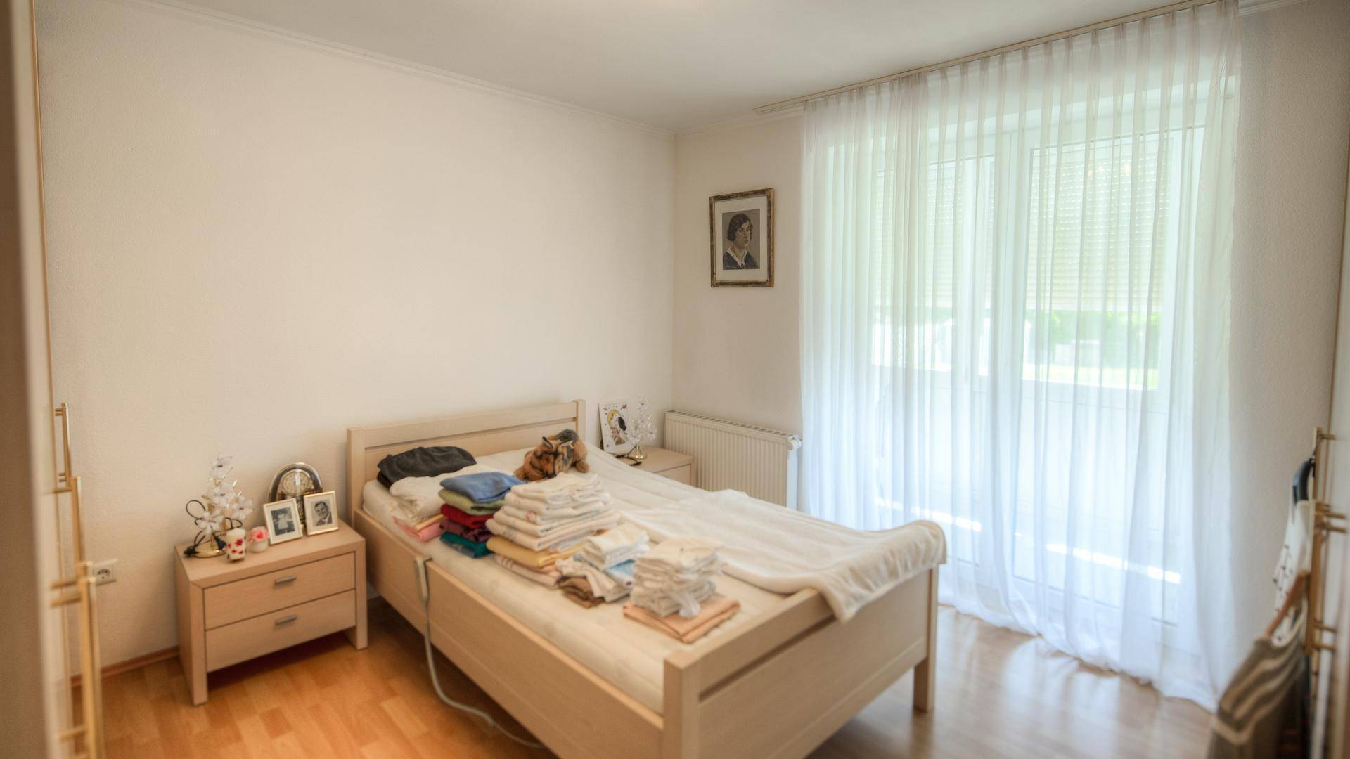 Schlafzimmer mit Doppelbett, Holzboden und großen Fenstern, die viel Licht hereinlassen.