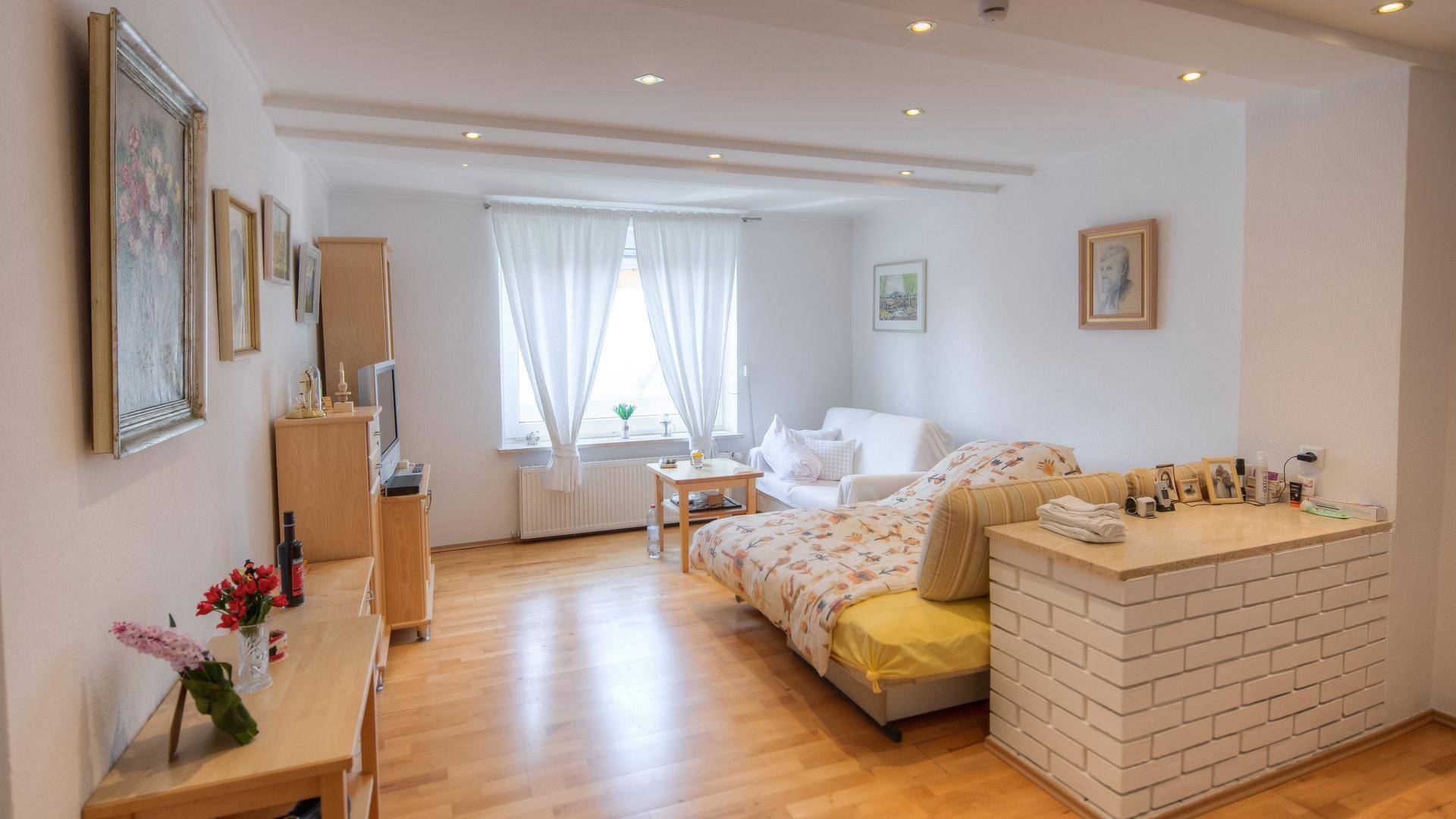 Helles Wohnzimmer mit beigem Sofa, Holzboden und einer dekorativen Ziegelwand als Raumteiler.