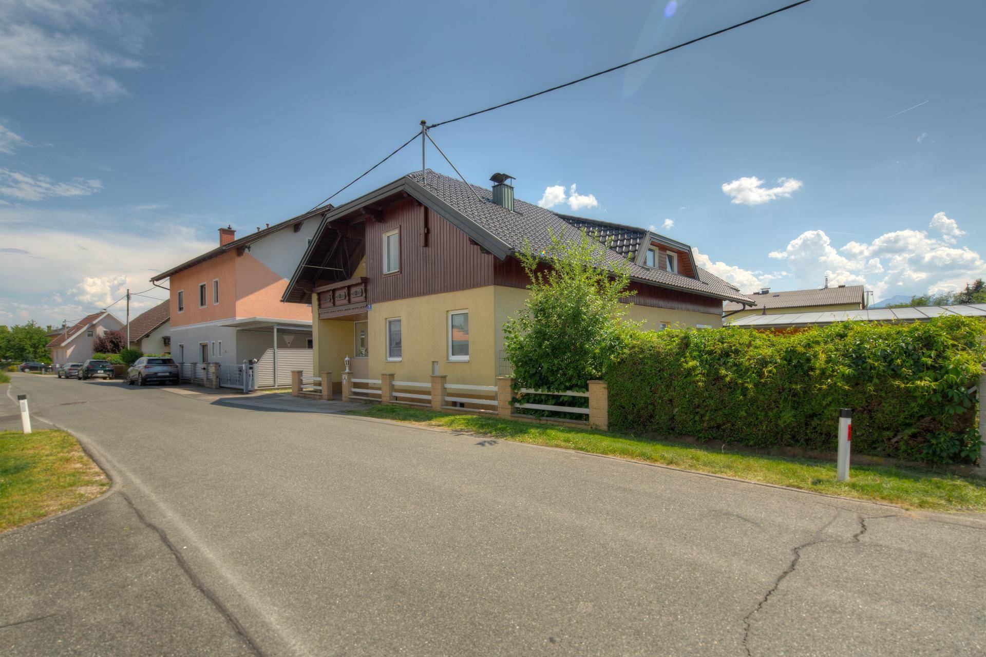 Seitenansicht des Hauses mit Dachgauben und umgebender Hecke unter blauem Himmel.