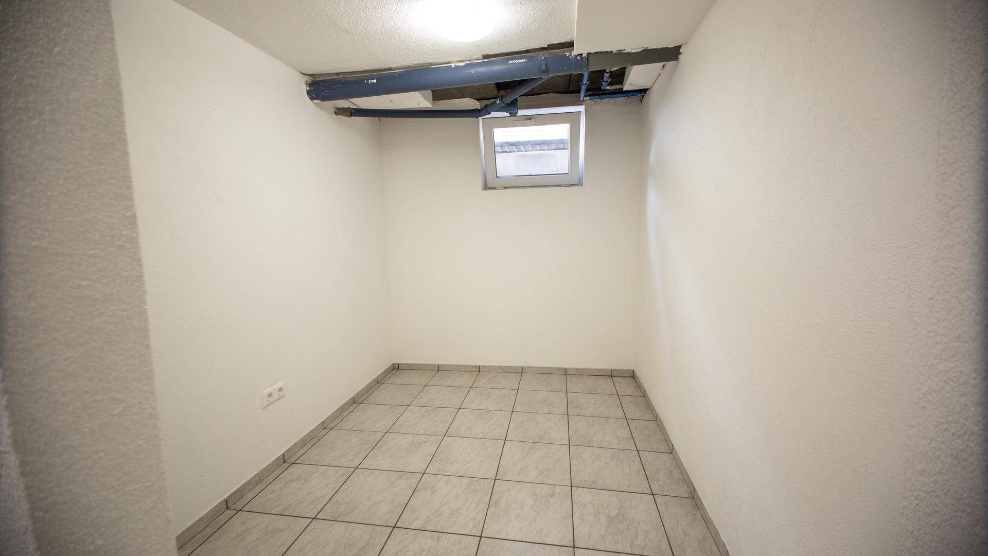 Funktionaler Kellerraum mit Fliesenboden und sichtbaren Installationen an der Decke.