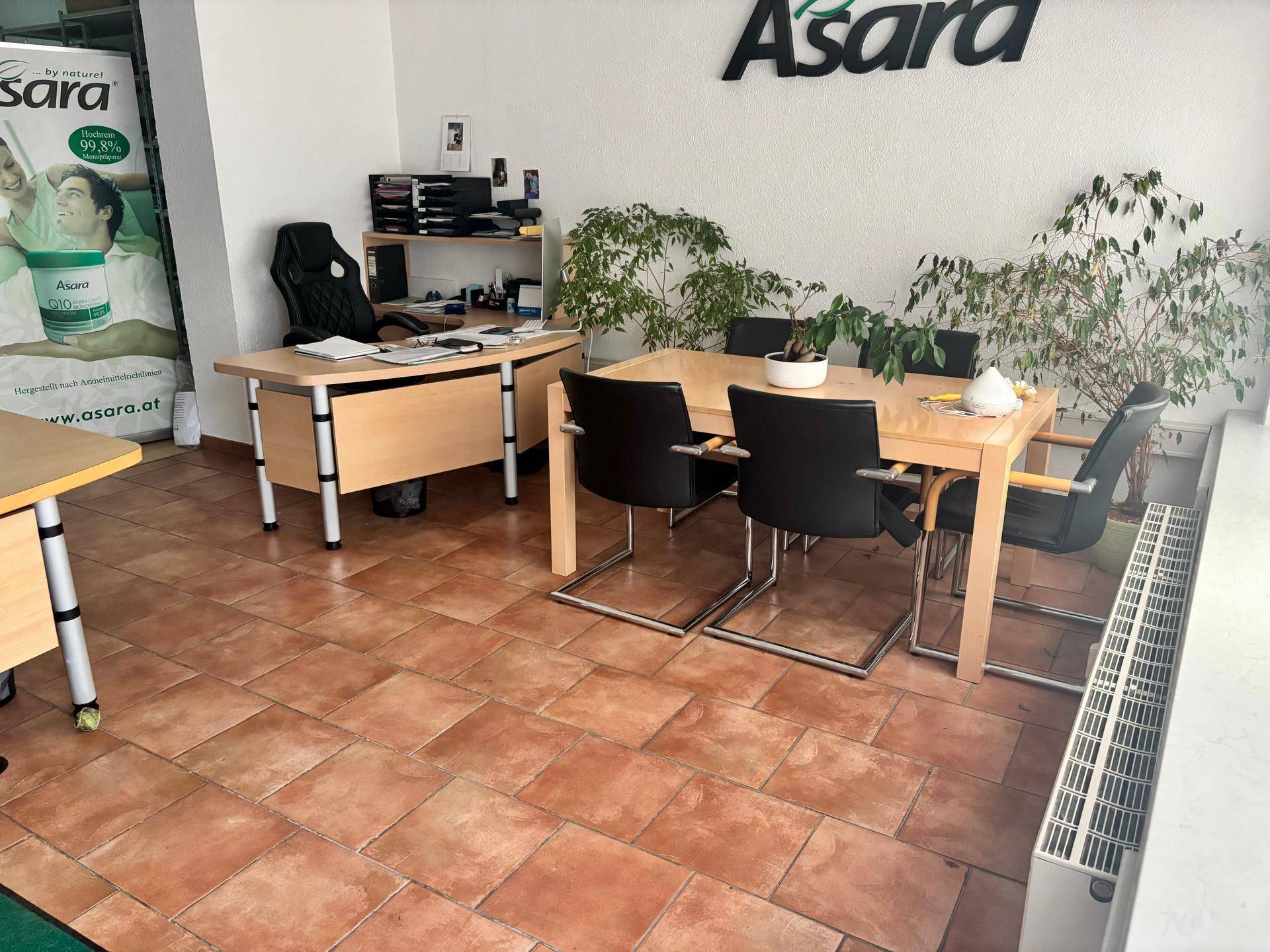 Bürobereich mit Besprechungstisch, Stühlen und Pflanzen, ebenfalls mit Terrakottafliesen und Heizkörper.