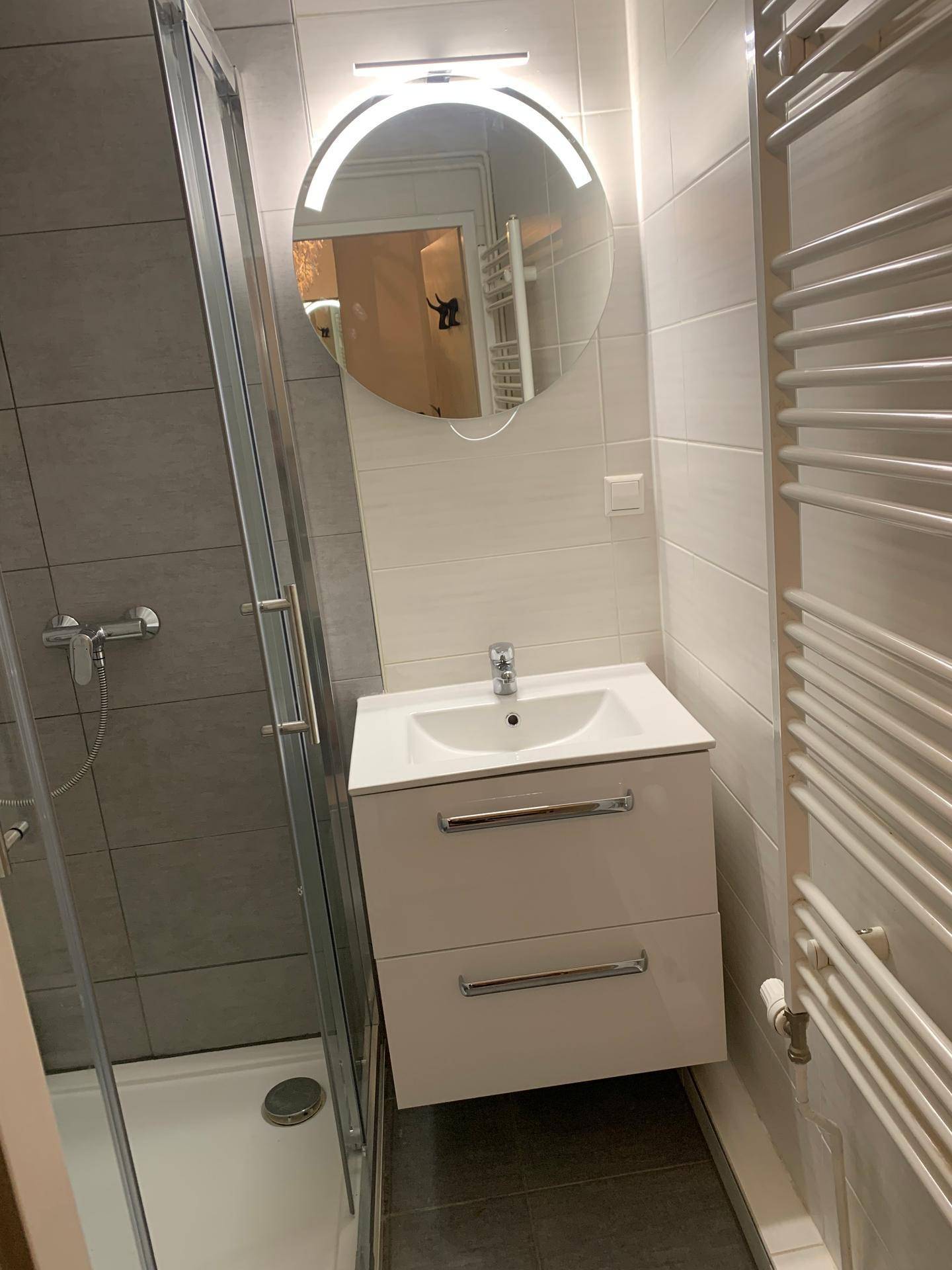 Modernes Badezimmer mit Duschkabine, Einzelwaschbecken und beleuchtetem Spiegel sowie Handtuchheizkörper.