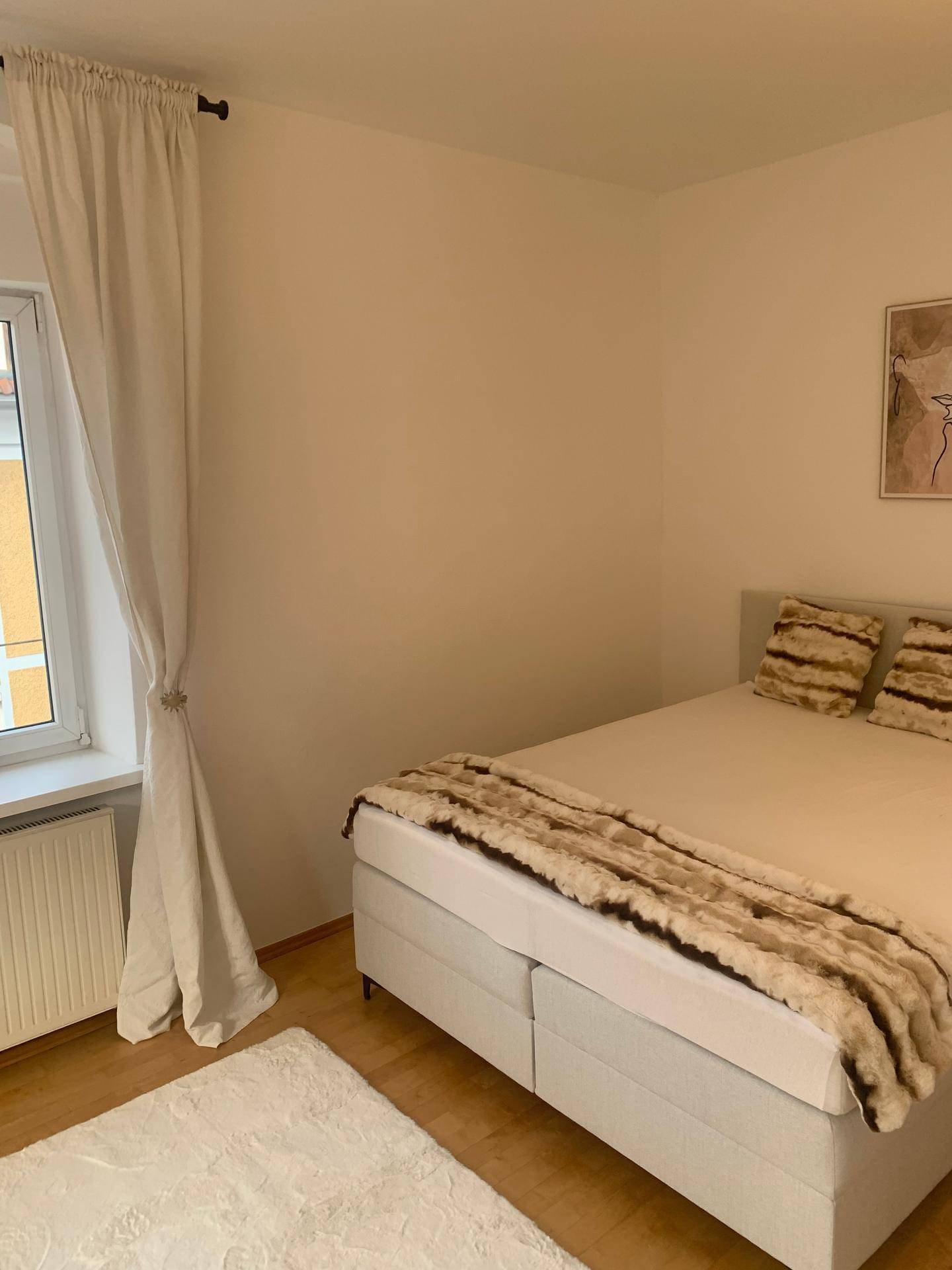 Schlafzimmer mit großem Bett, hellem Fenster und weichem Teppich auf dem Holzboden.