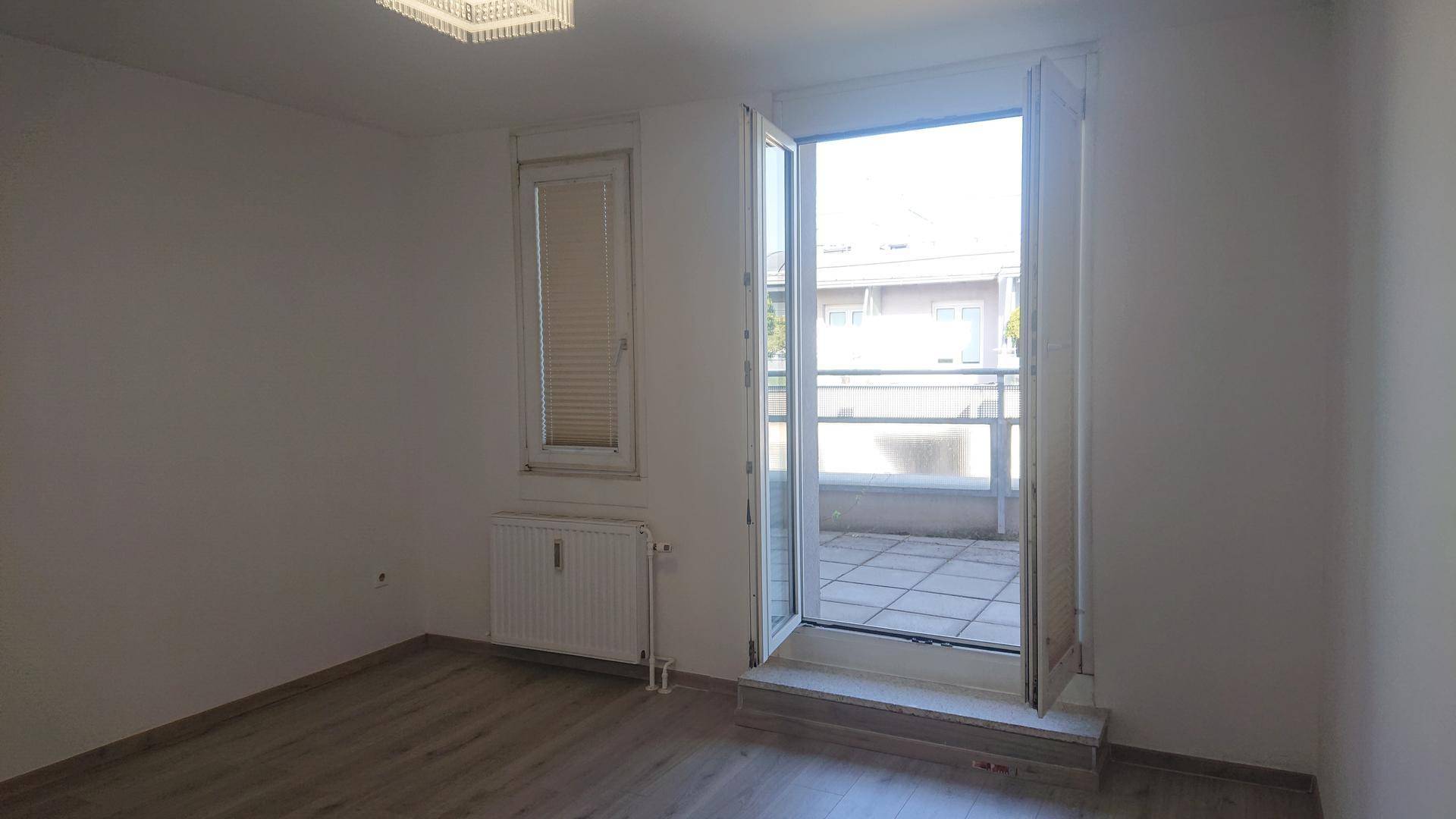 Heller Raum mit Laminatboden, Heizkörper und direktem Zugang zu einem Außenbereich.