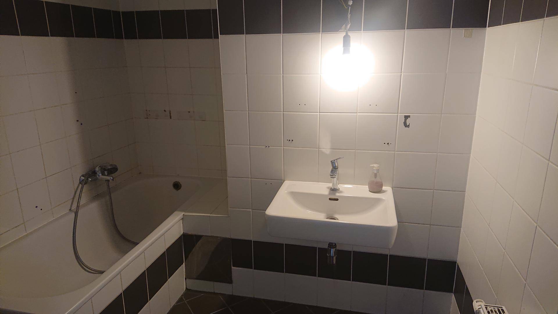 Badezimmer mit schwarz-weißen Fliesen, einer Badewanne und einem Waschbecken.