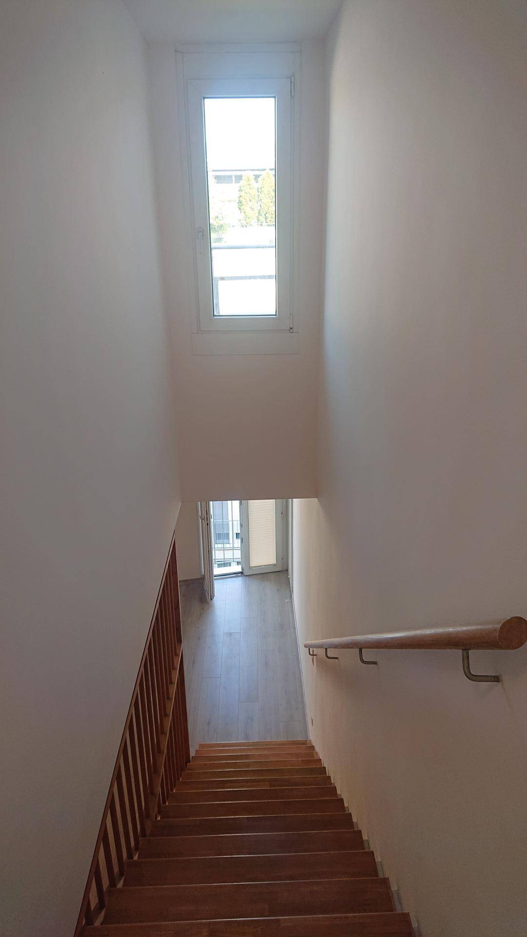 Holztreppe führt nach unten, mit einem Fenster am oberen Treppenabsatz für natürliches Licht.