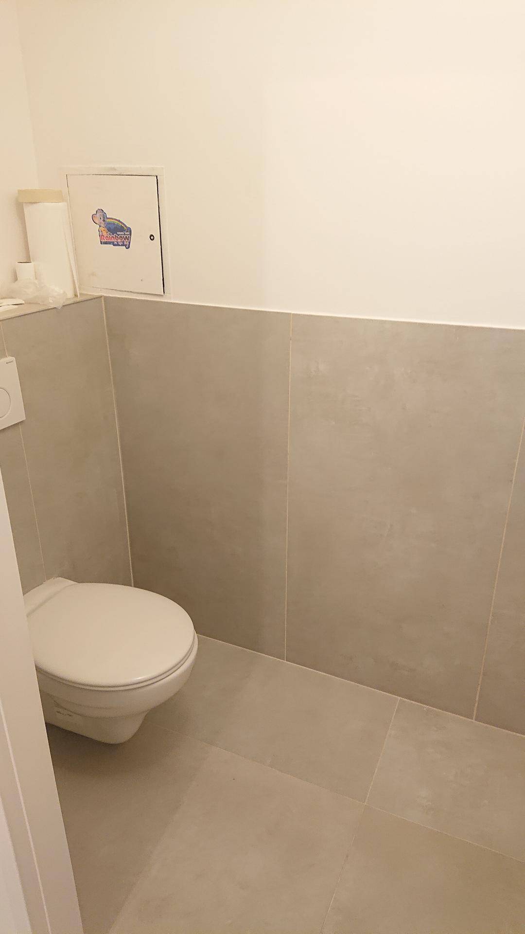 Gäste-WC mit wandhängender Toilette und beigefarbenen Fliesen an Boden und Wänden.