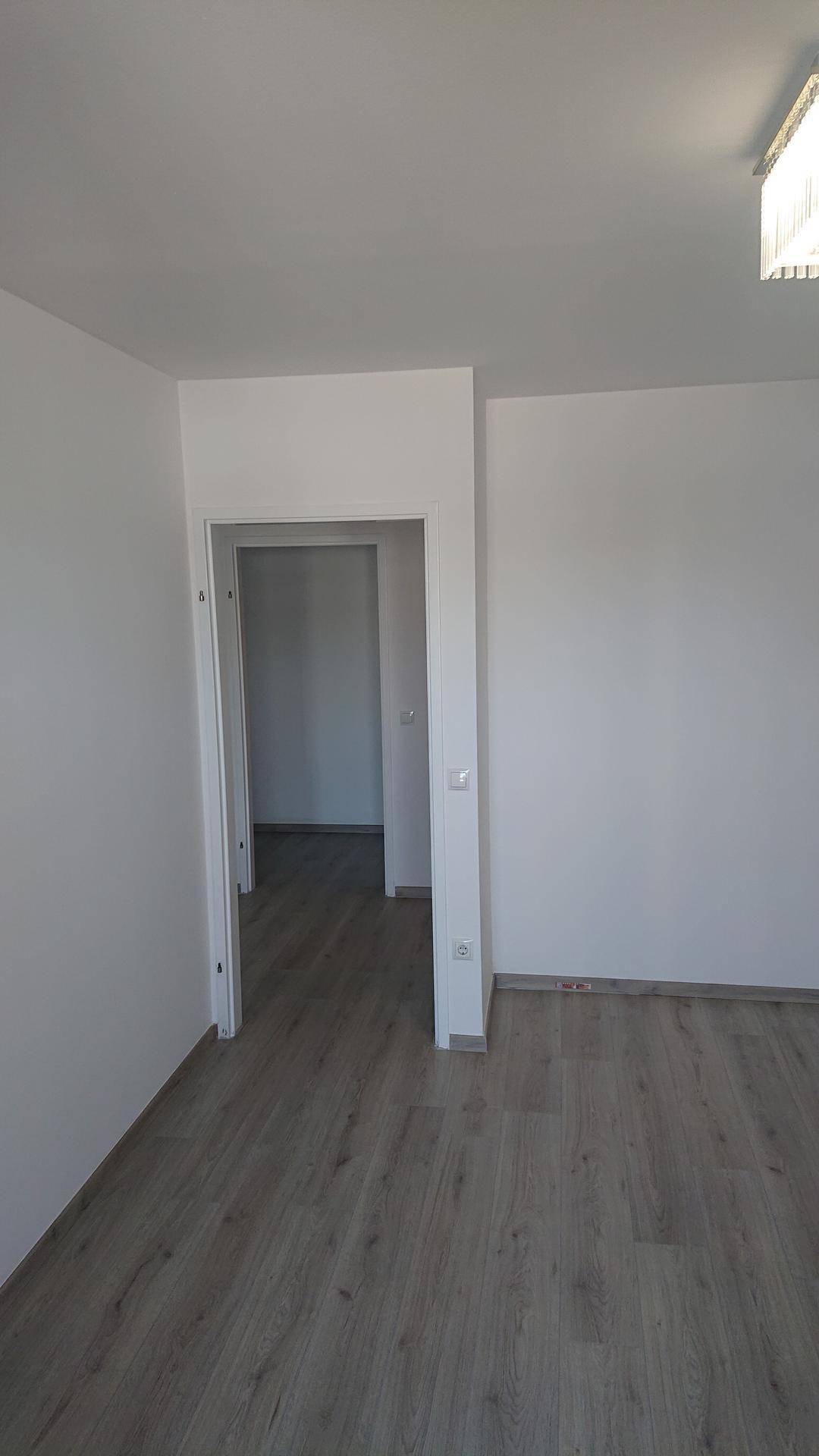 Leerer Raum mit hellem Laminatboden und weiß gestrichenen Wänden, bereit zur Einrichtung.