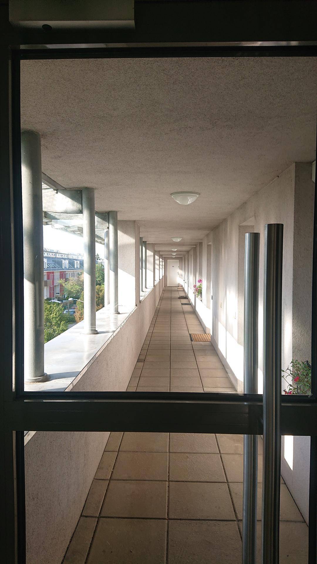 Langer, überdachter Außenflur mit Säulen und Fliesenboden, bietet Blick auf die Umgebung.