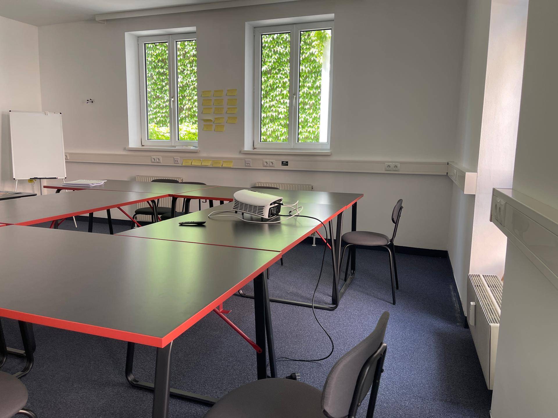 Blick auf den Konferenzraum mit Tischen, Stühlen und Fenstern, die viel Tageslicht hereinlassen.