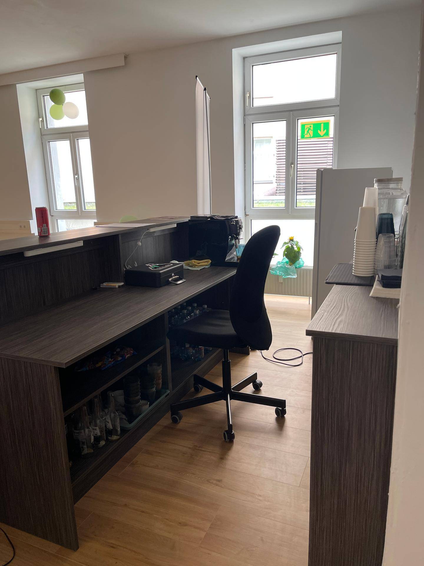 Empfangsbereich mit dunklem Holzschreibtisch, Bürostuhl und Fenstern, die den Raum erhellen.