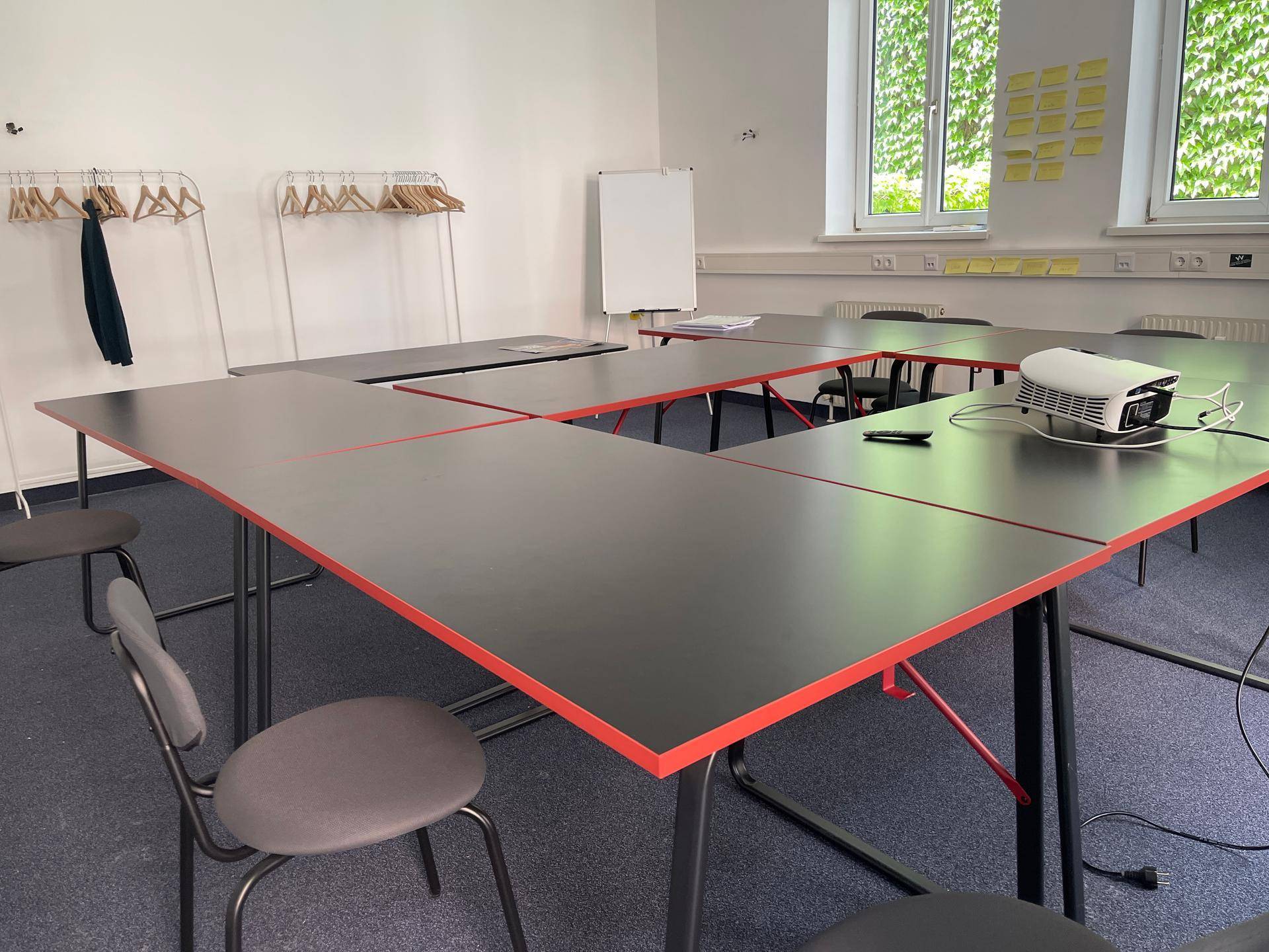 Nahaufnahme des Konferenzraums mit Projektor auf dem Tisch und Kleiderständern im Hintergrund.