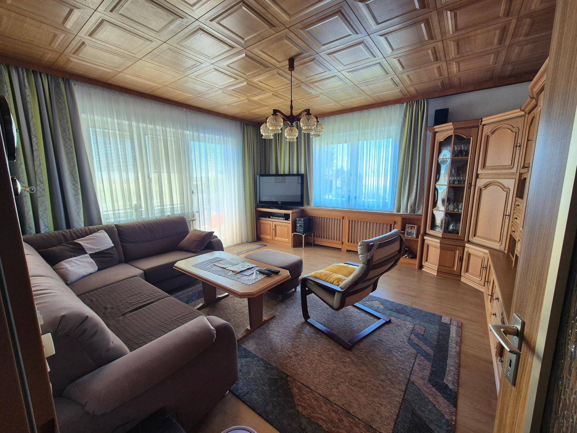 Gemütliches Wohnzimmer mit Holzkassettendecke, Teppichboden und traditionellen Möbeln.