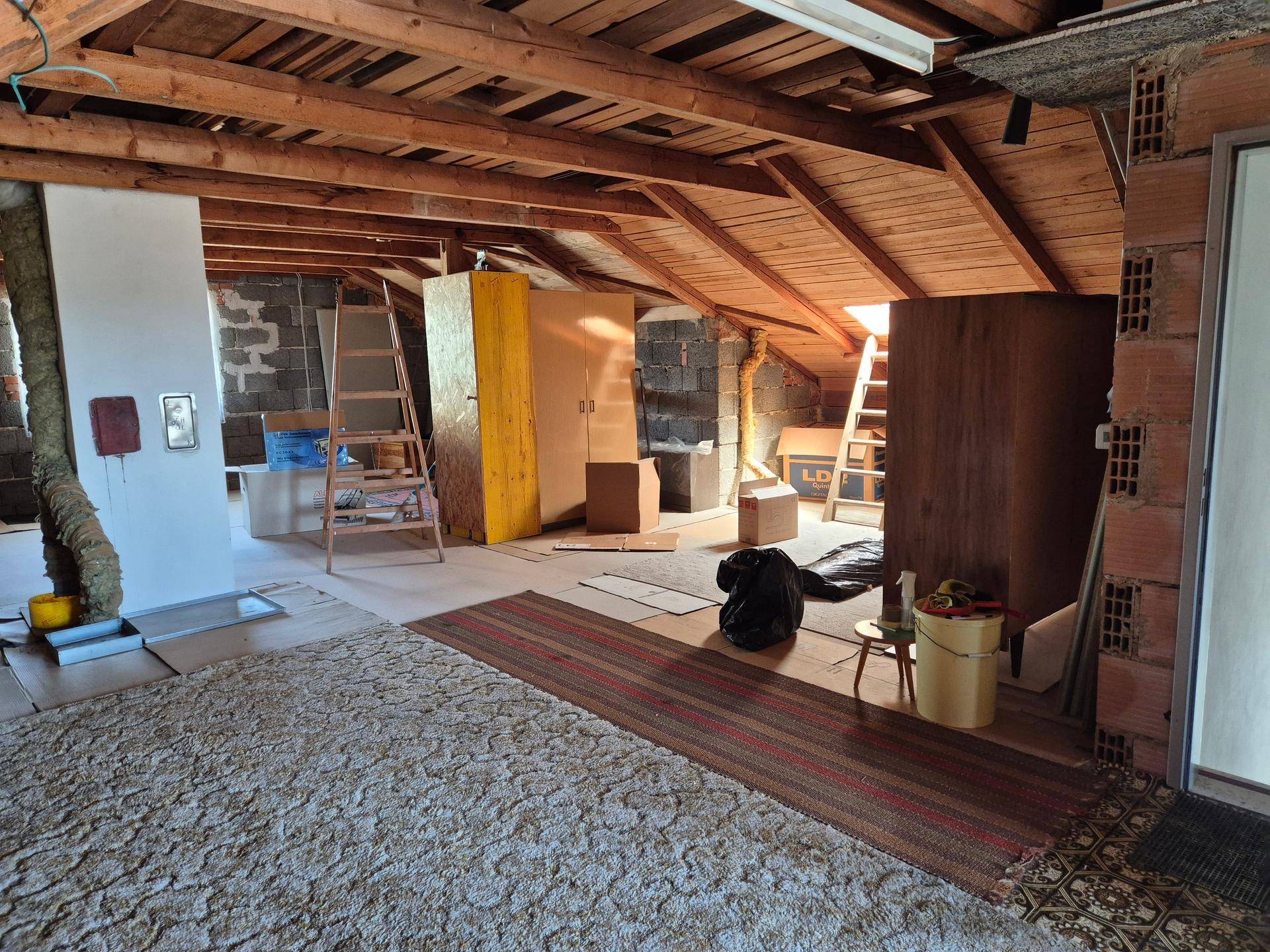 Ausbaufähiger Dachboden mit sichtbaren Holzbalken und Teppichboden.