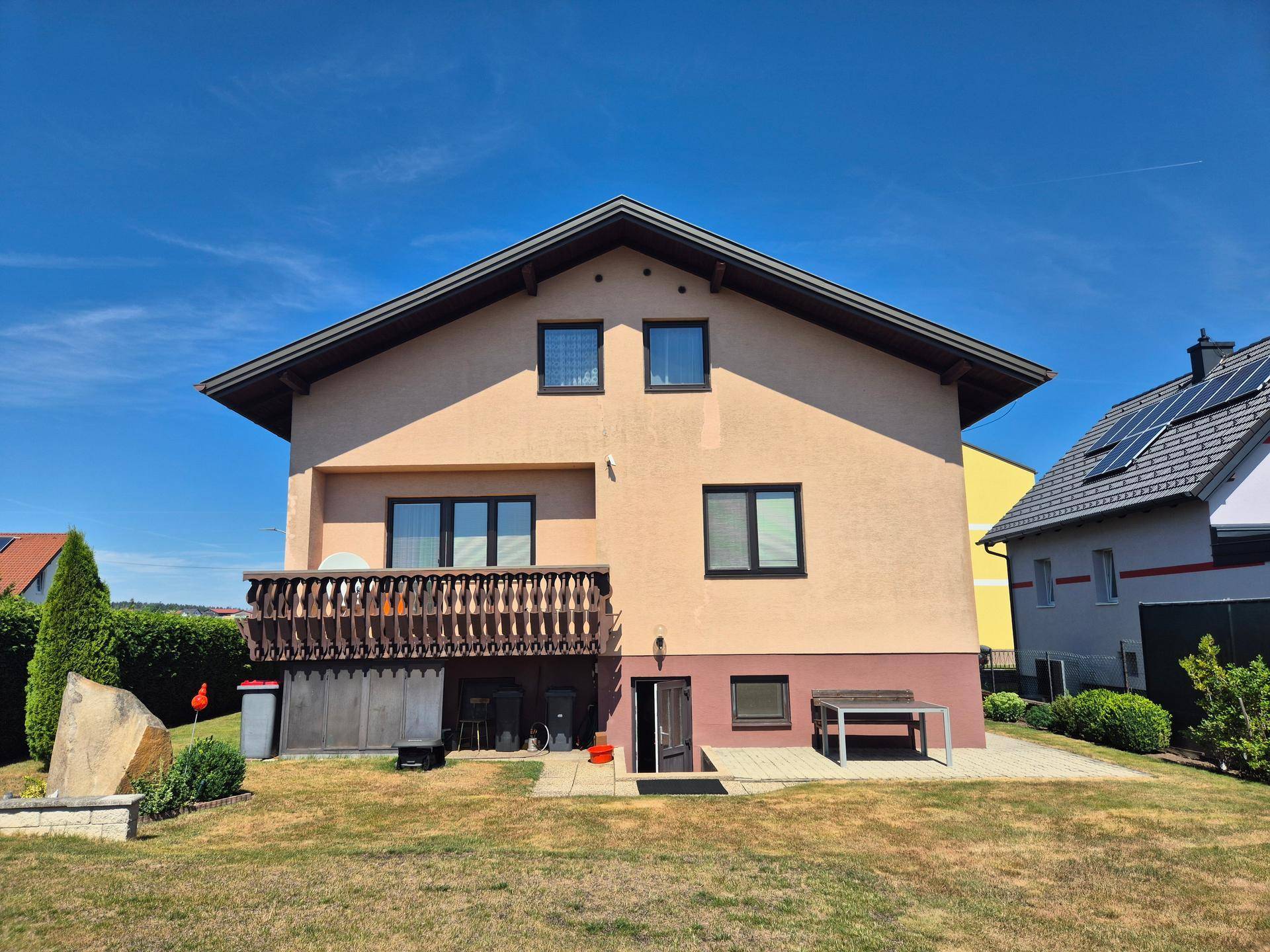 Rückansicht des Hauses mit Balkon und Gartenbereich unter strahlend blauem Himmel.