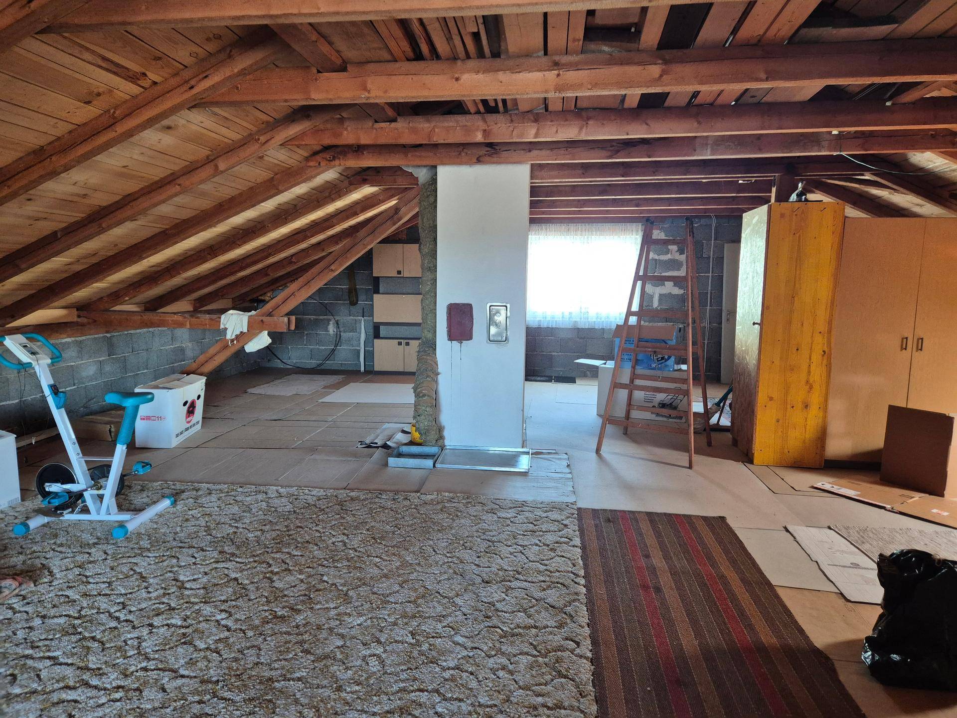 Unfertiger Dachboden mit sichtbaren Holzbalken und Teppichboden, bereit für den Ausbau.
