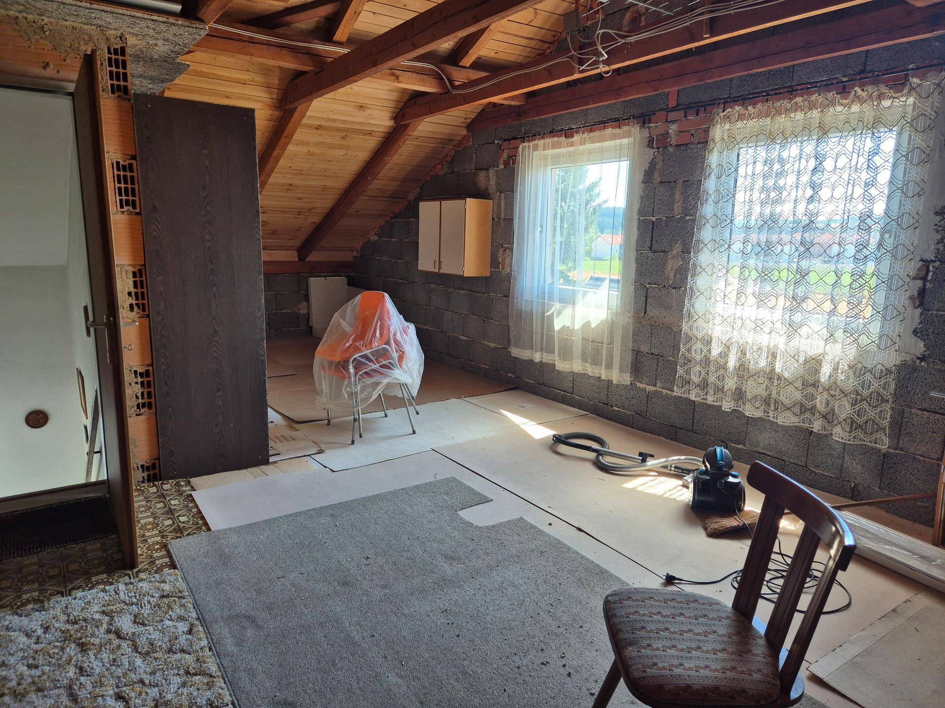 Heller Dachboden mit zwei Fenstern, sichtbaren Holzbalken und unverputzten Wänden, ideal für Ausbau.