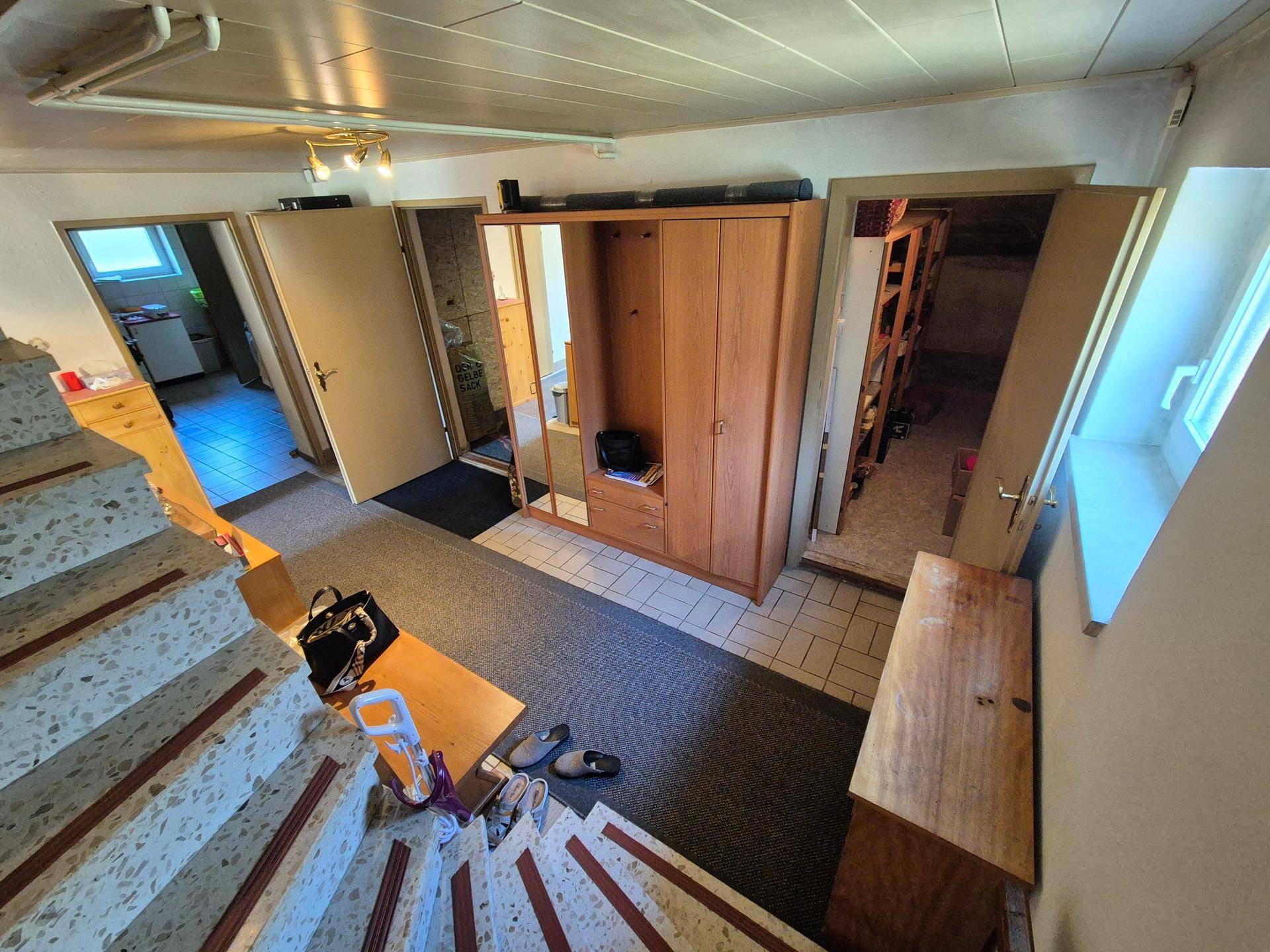 Treppenhaus und Flur im Untergeschoss mit Fliesenboden und Holzschrank.