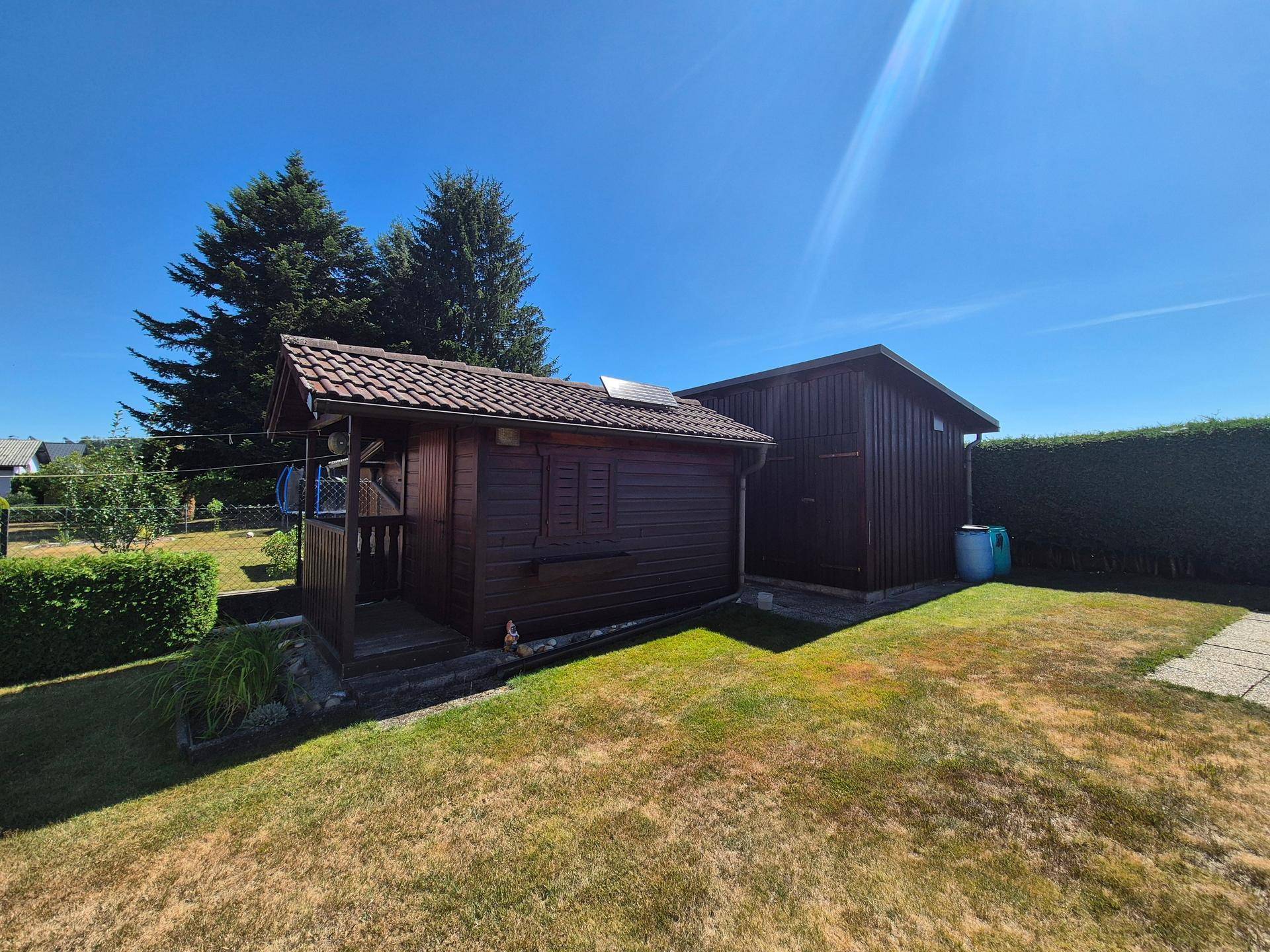 Garten mit zwei Holzschuppen und gepflegter Rasenfläche unter blauem Himmel.