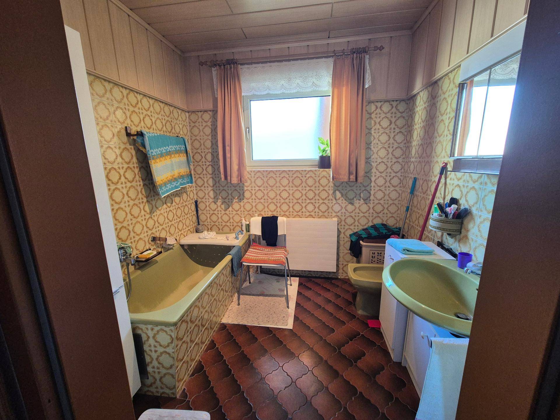 Badezimmer im 80er-Jahre-Stil mit grüner Badewanne, gemusterten Fliesen und Fenster.