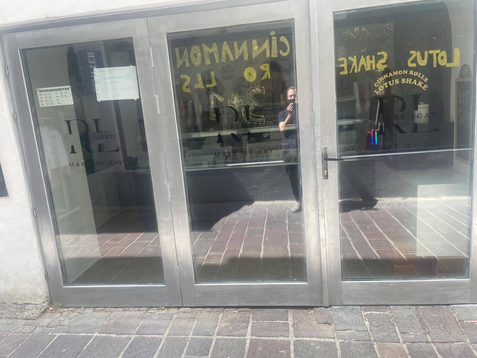 Außenansicht eines Geschäfts mit großen Glastüren und reflektierenden Schaufenstern zur Straße hin.
