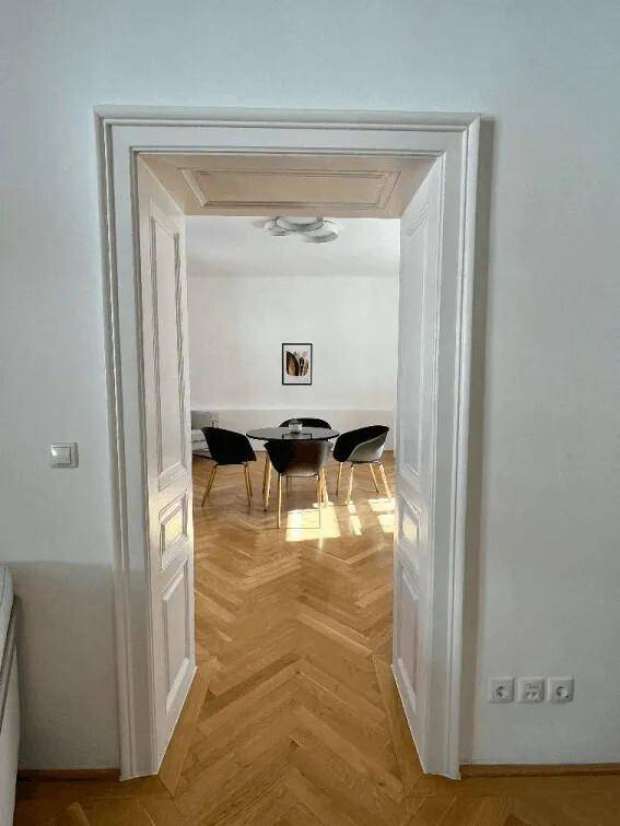 Blick durch eine weiße Tür in einen hellen Raum mit Tisch und Stühlen.