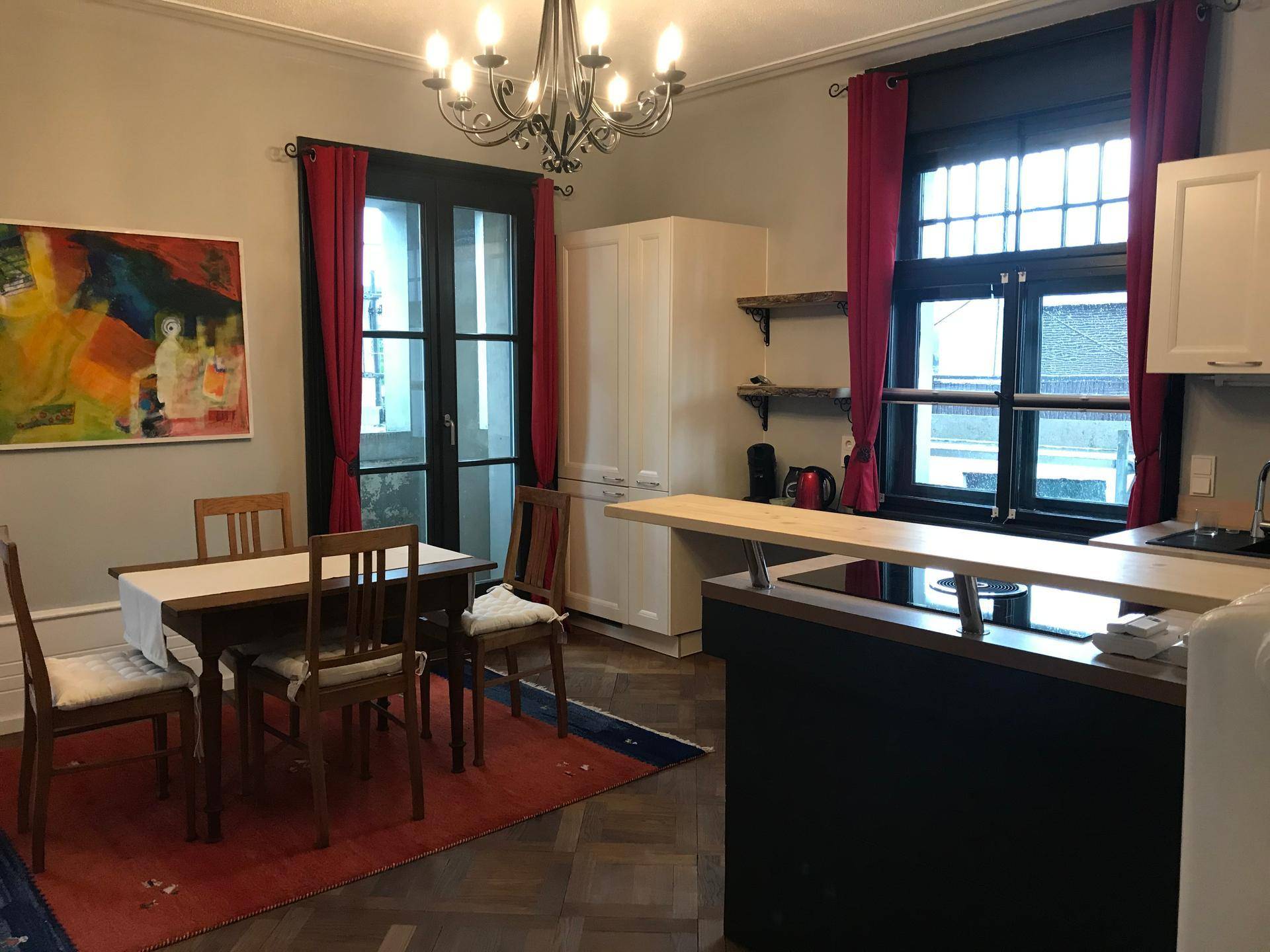 Offene Wohnküche mit Esstisch, Küchenzeile und Bartresen, beleuchtet durch große Fenster.