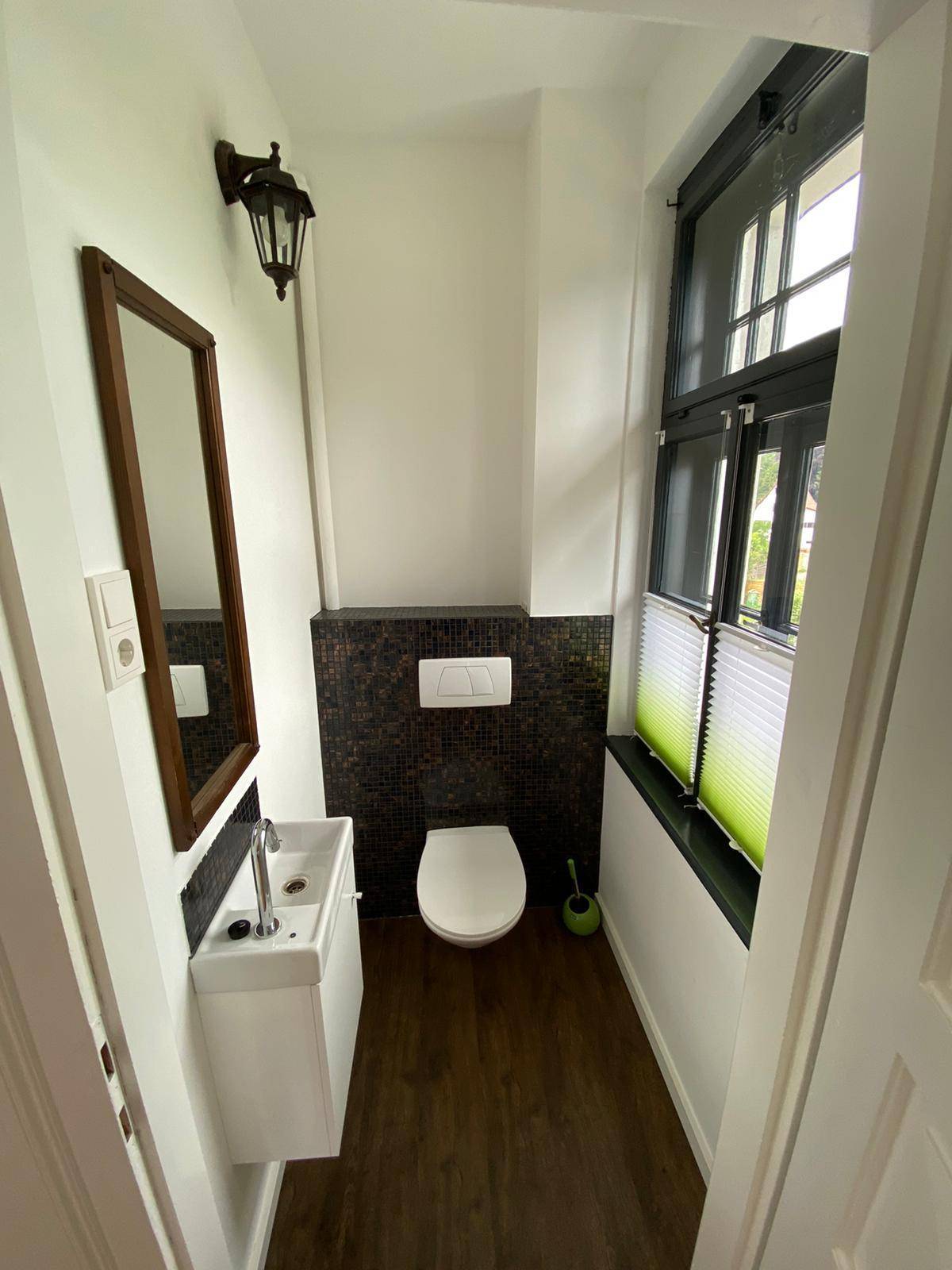 Kleines Gäste-WC mit modernem Wand-WC, Waschbecken und einem Fenster für natürliche Belüftung.