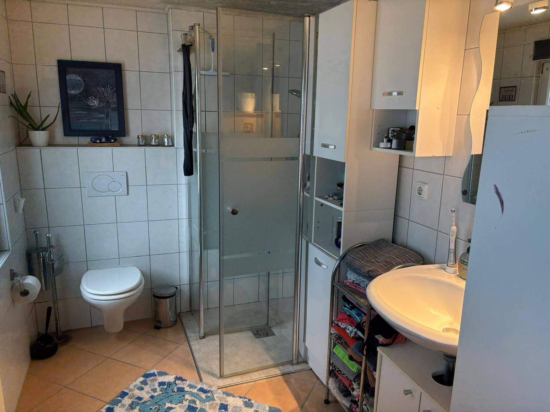 Badezimmer mit Duschkabine, wandhängendem WC, Waschbecken und hellen Fliesen an Wänden und Boden.