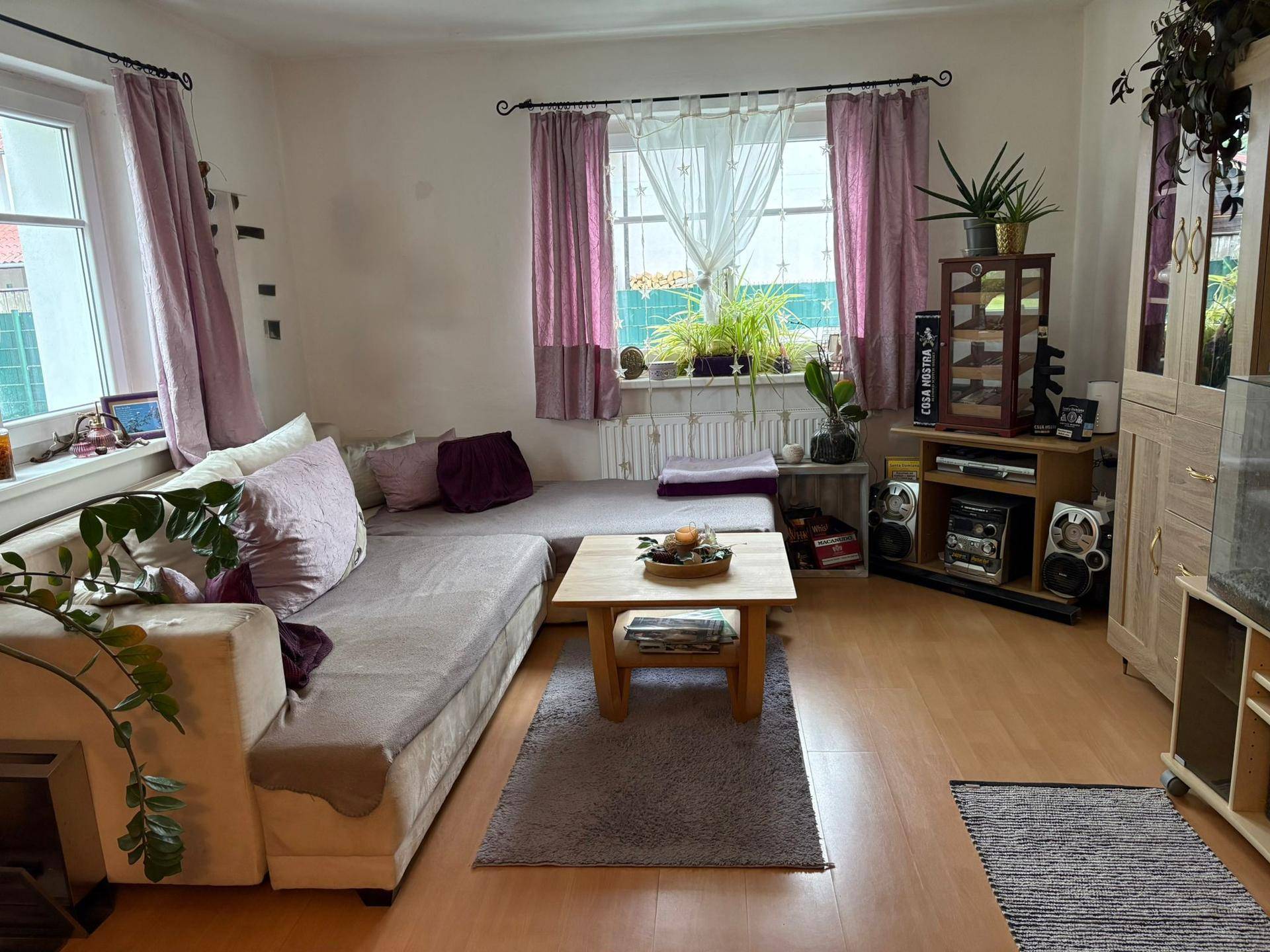 Helles Wohnzimmer mit großem Sofa, Couchtisch und Fenstern, die viel Tageslicht hereinlassen.