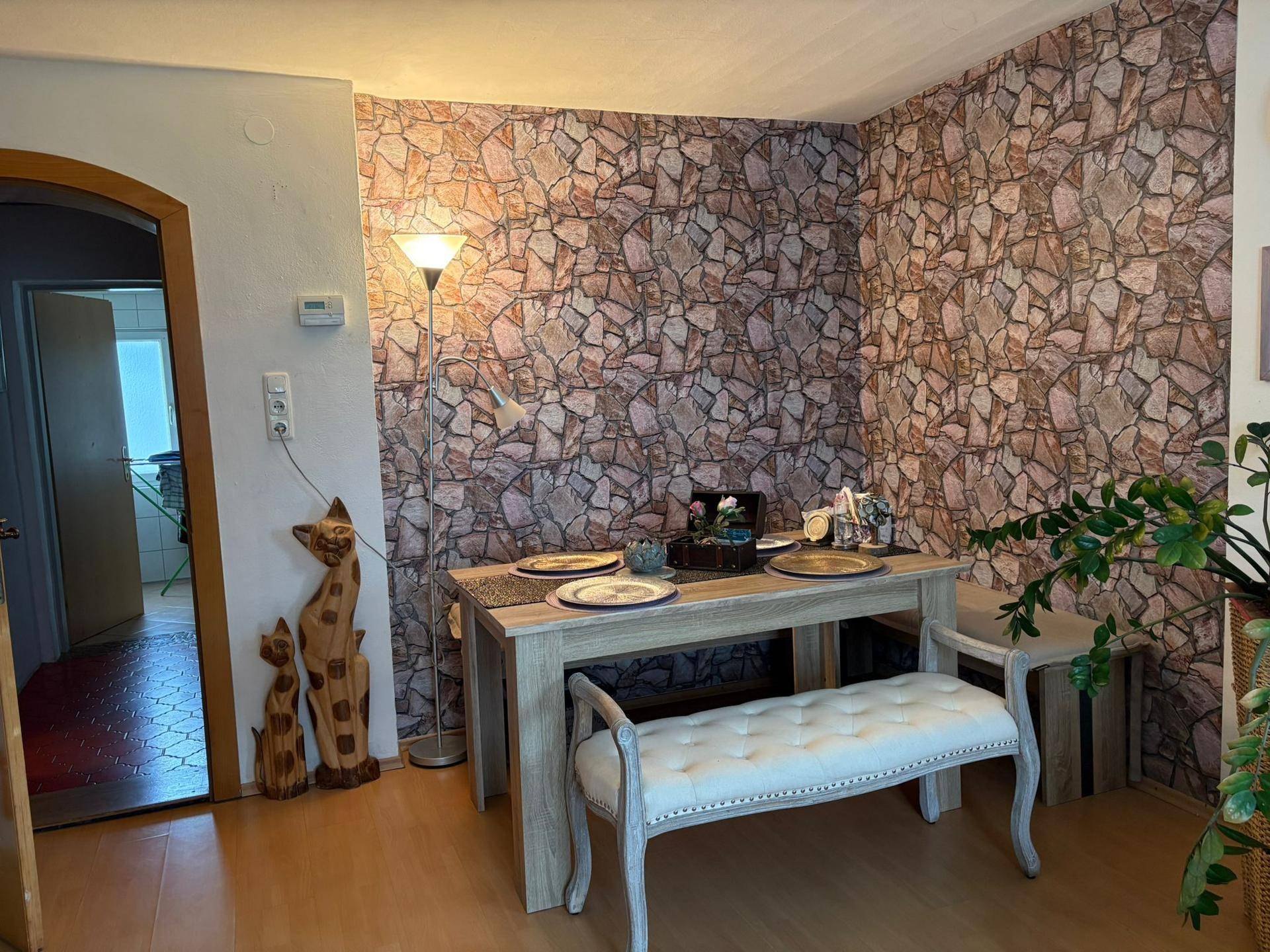 Gemütlicher Essbereich mit Holztisch, gepolsterter Bank und einer Wand mit Steinmuster-Tapete.