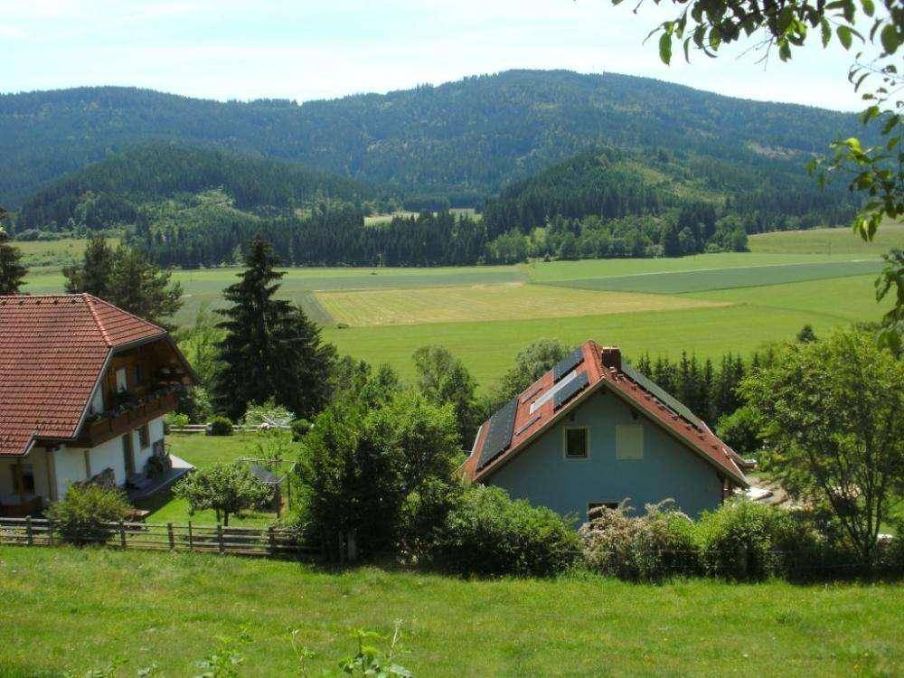 Idyllische Landschaft mit Häusern, grünen Feldern und einer Bergkette am Horizont.