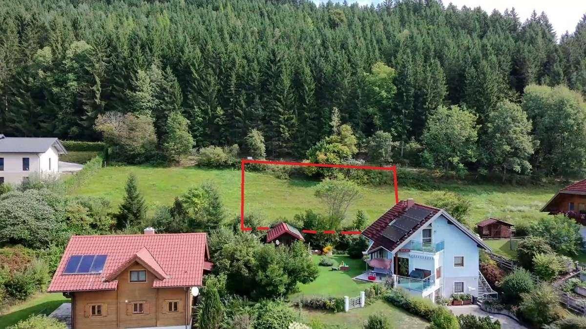 Luftaufnahme eines Grundstücks mit roter Umrandung, umgeben von Wald und Wohnhäusern.