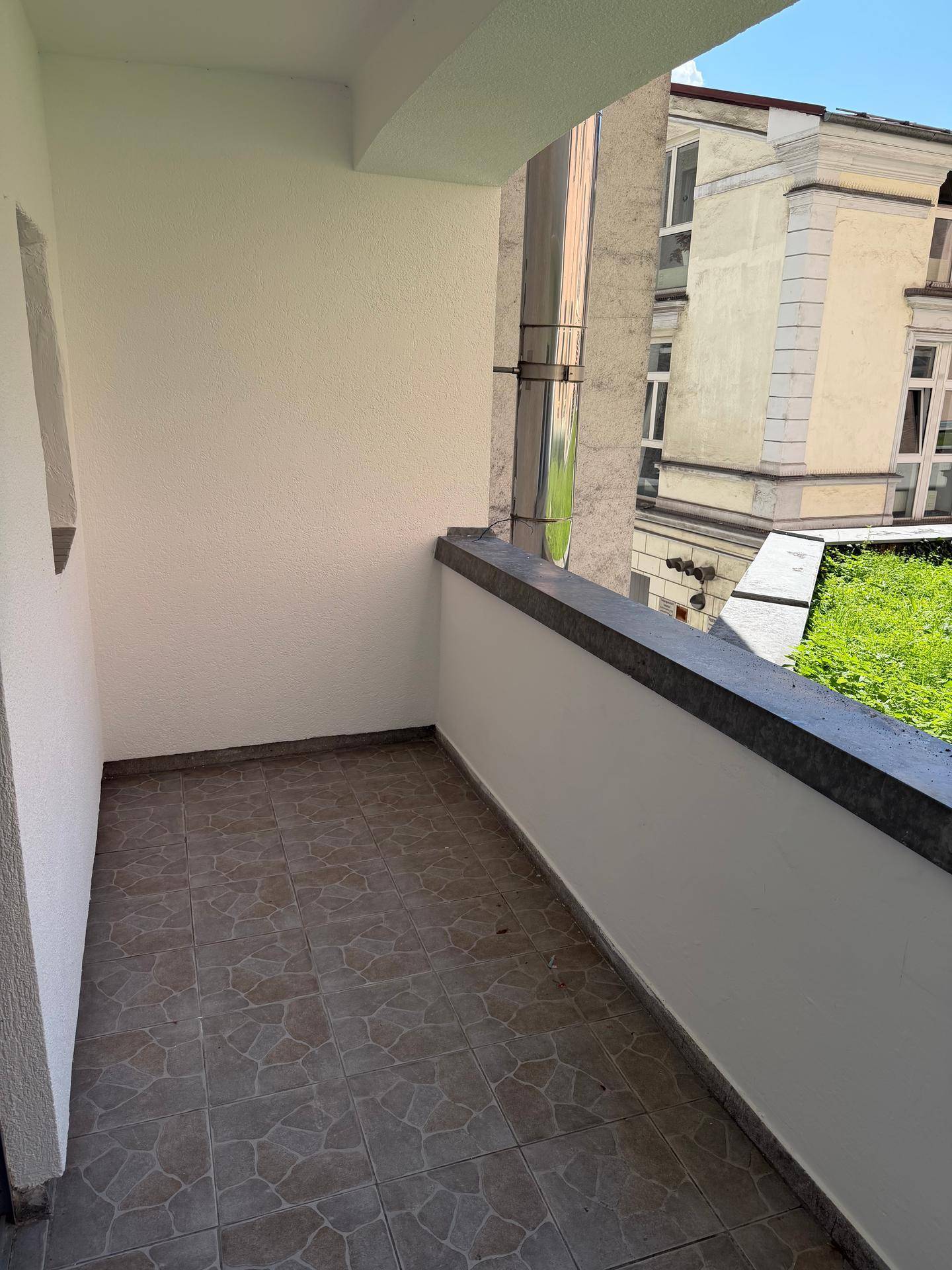 Kleiner Balkon mit Fliesenboden und Blick auf ein historisches Gebäude und etwas Grün.