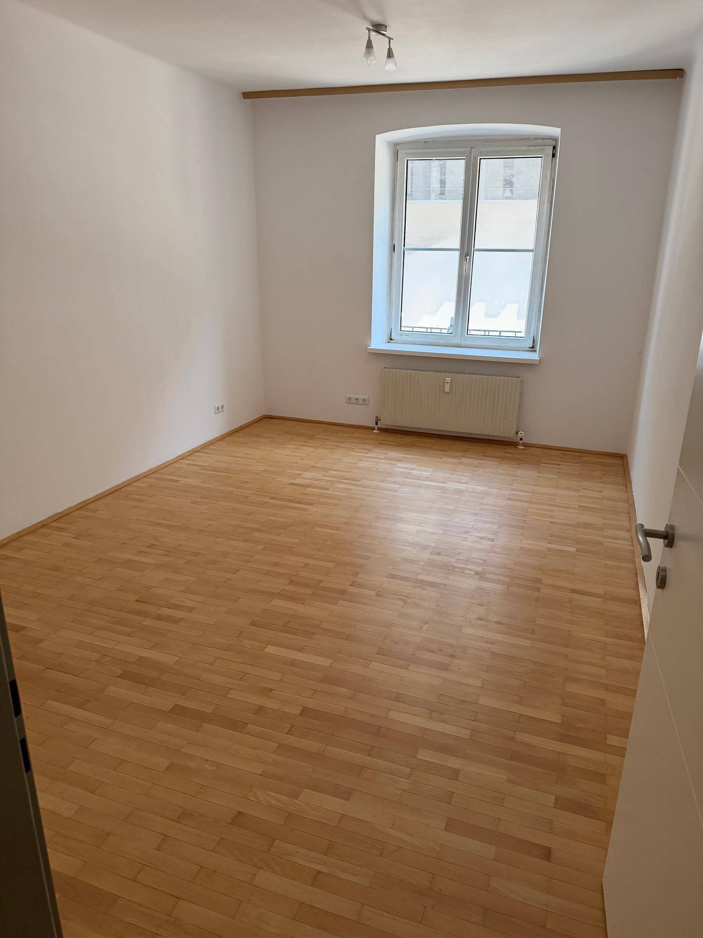 Helles Schlafzimmer mit Parkettboden, weißen Wänden und einem großen Fenster mit Stadtblick.