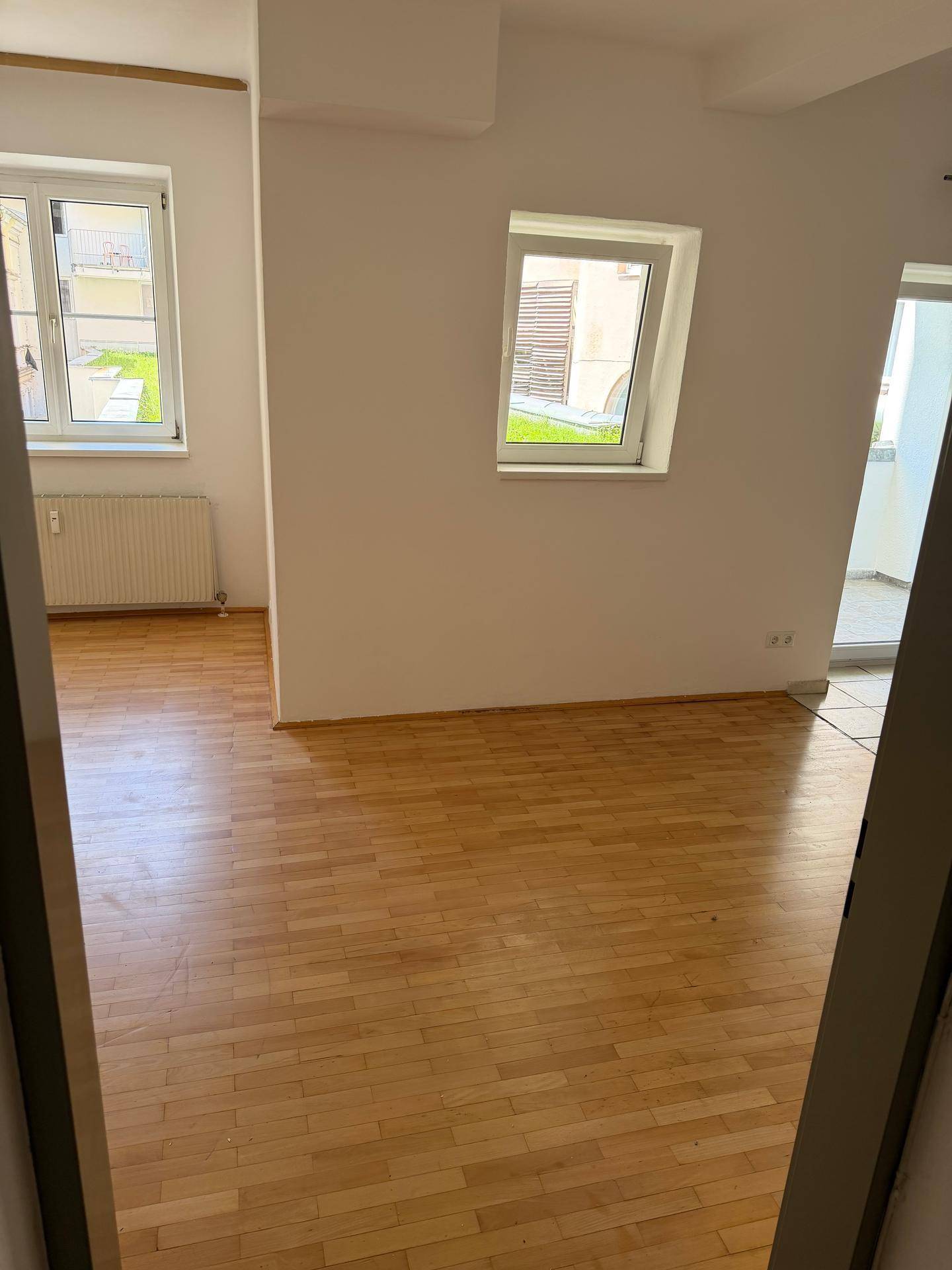 Heller Raum mit Parkettboden, weißen Wänden und mehreren Fenstern, die viel Tageslicht hereinlassen.