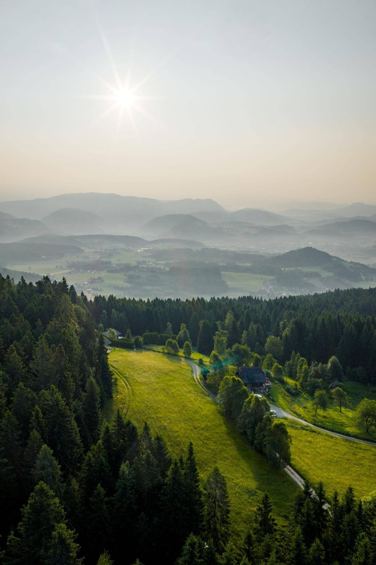 Malerische Landschaft mit bewaldeten Hängen, einem Haus auf einer Lichtung und weitem Talblick.