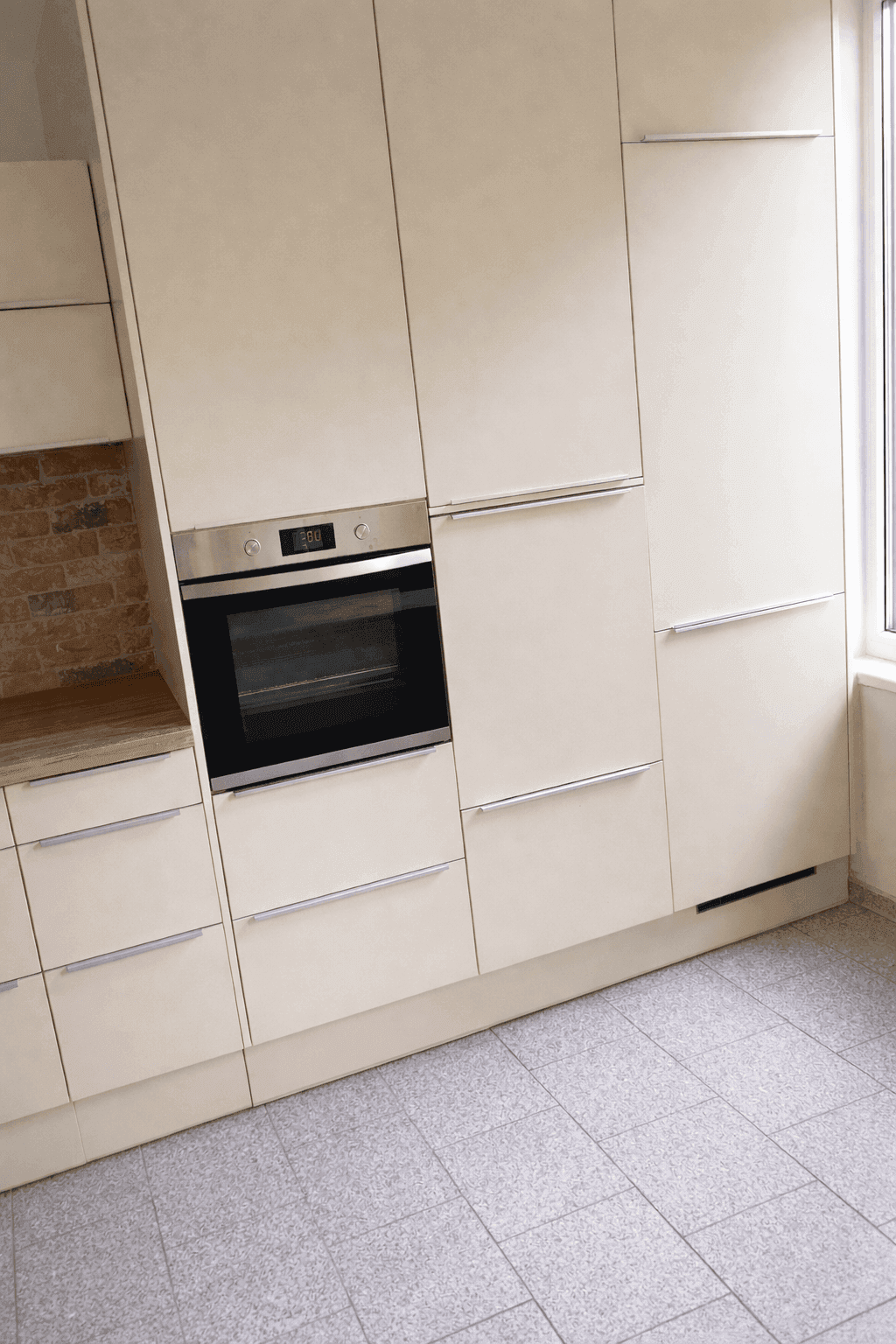 Helle Einbauküche in Beige mit integriertem Backofen und Fliesenboden.