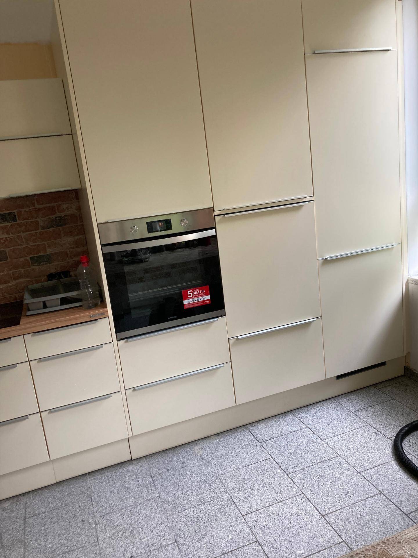 Moderne Einbauküche in Beige mit integriertem Backofen und Fliesenboden.