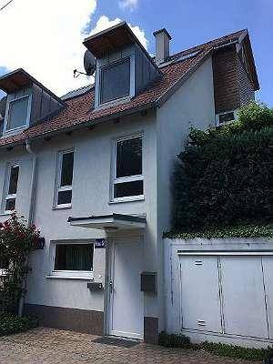 Reihenhausfassade mit Dachgauben, roten Ziegeln und gepflegter Bepflanzung.