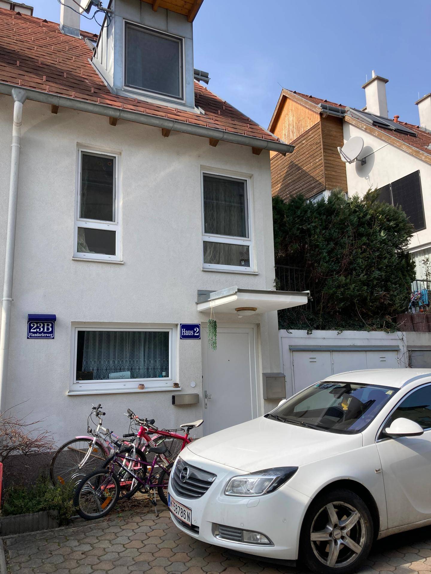 Reihenhausfassade mit Eingangsbereich, Fahrrädern und geparktem Auto.