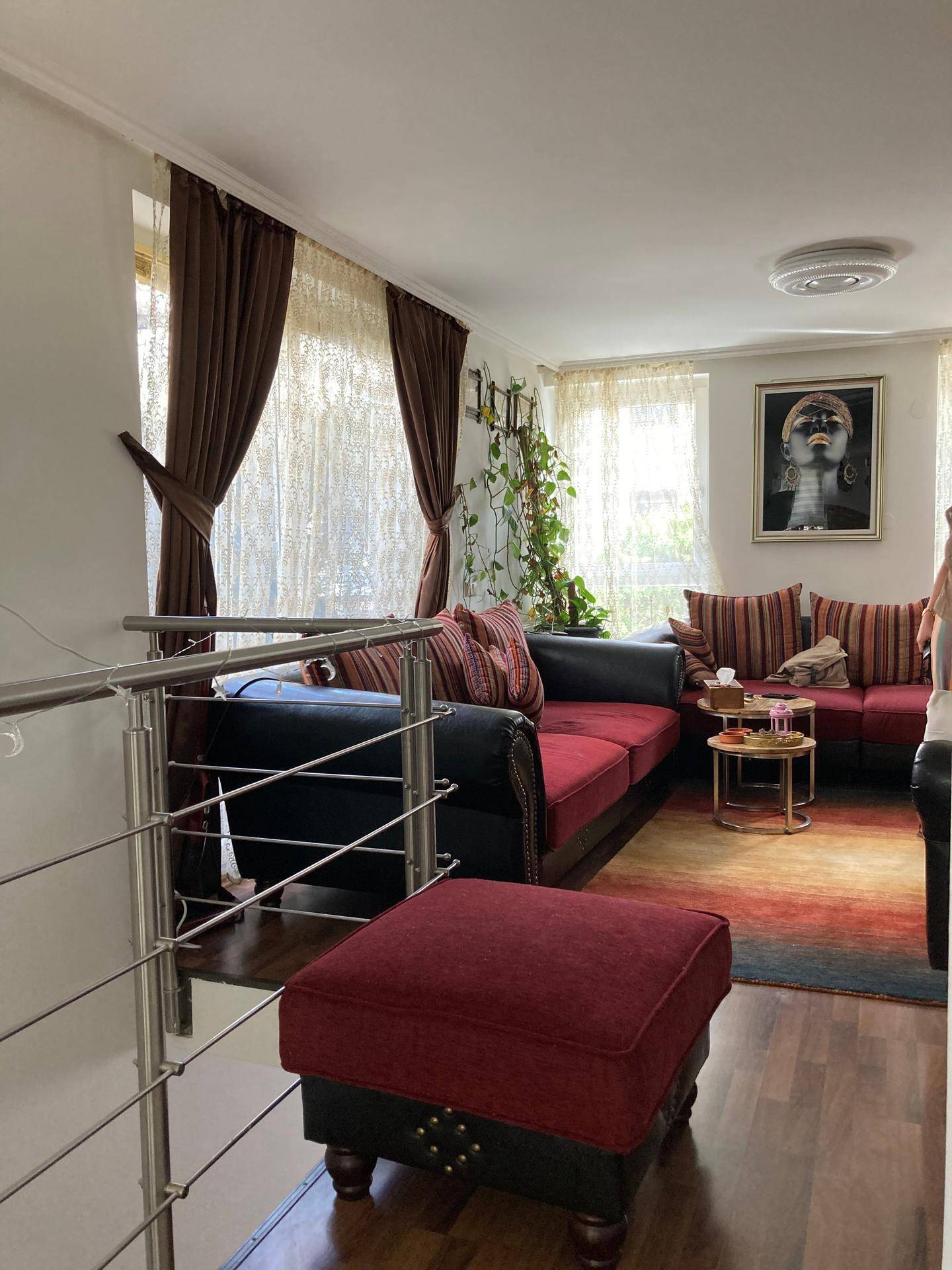 Gemütliches Wohnzimmer mit rotem Sofa, Holzboden und viel Tageslicht.